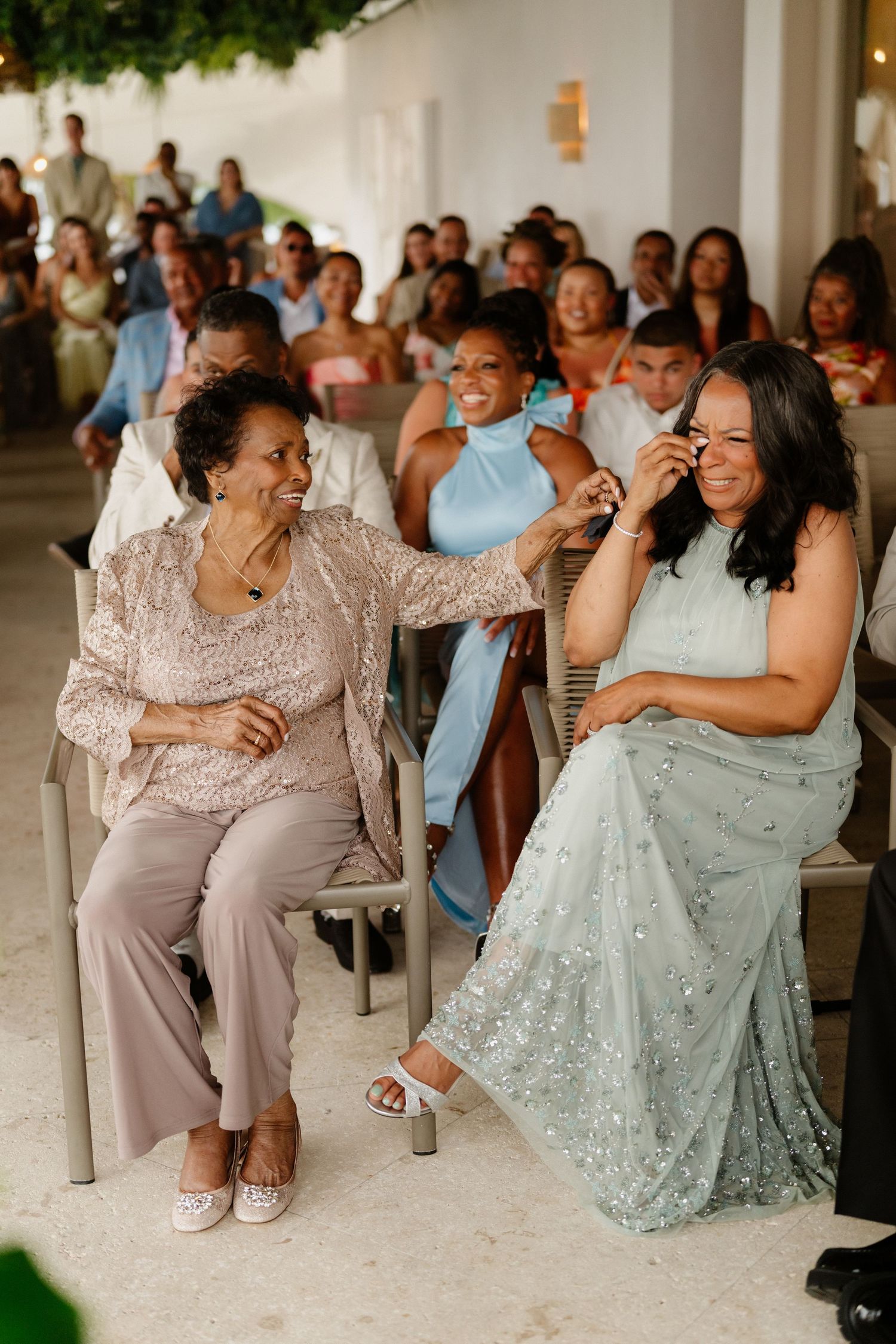 Two women smile and comfort each other emotionally while seated at wedding ceremony. Barbados photographer