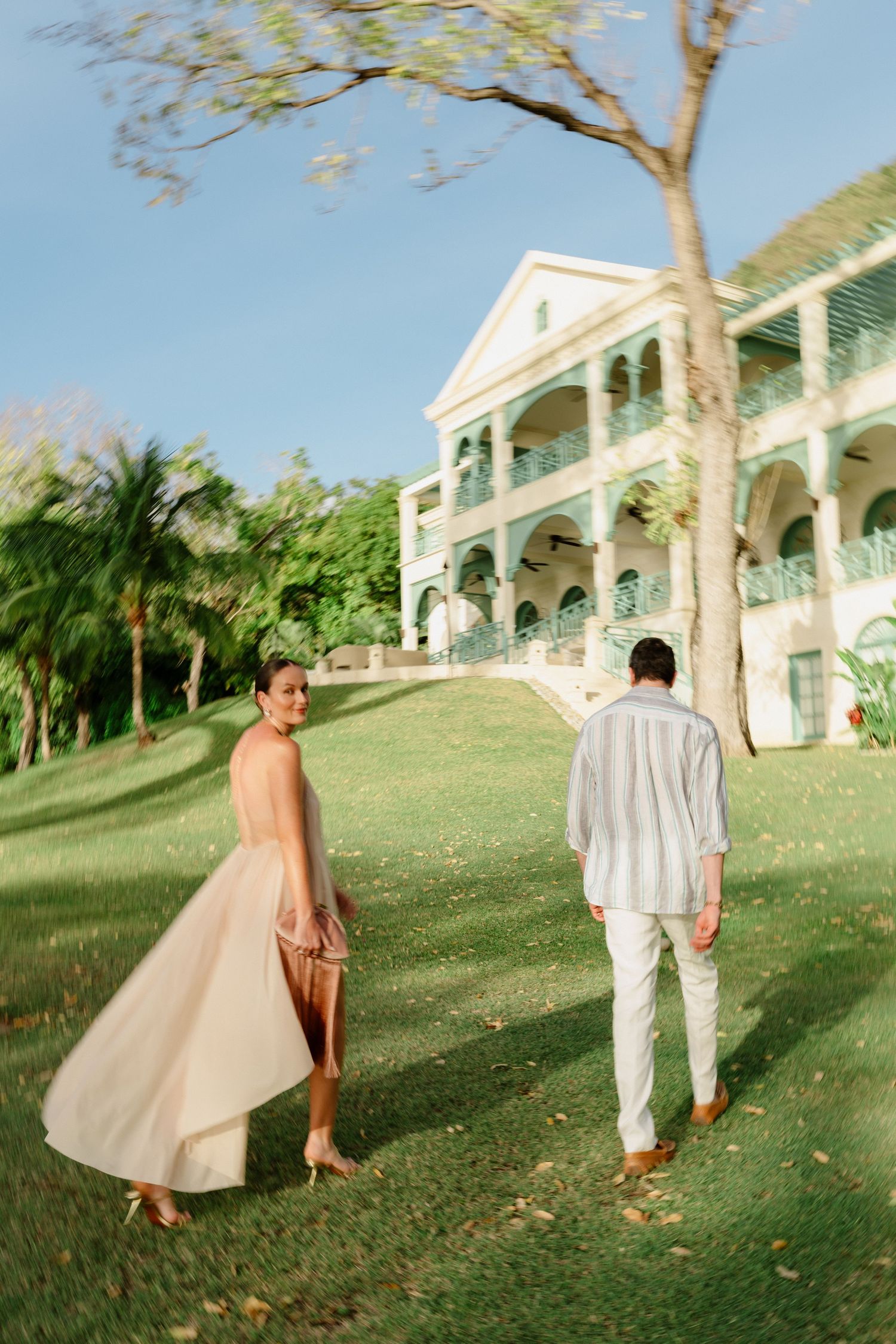 Couple strolling on lush green lawn before a grand colonial-style Caribbean estate on a sunny day. St Lucia Wedding photographer