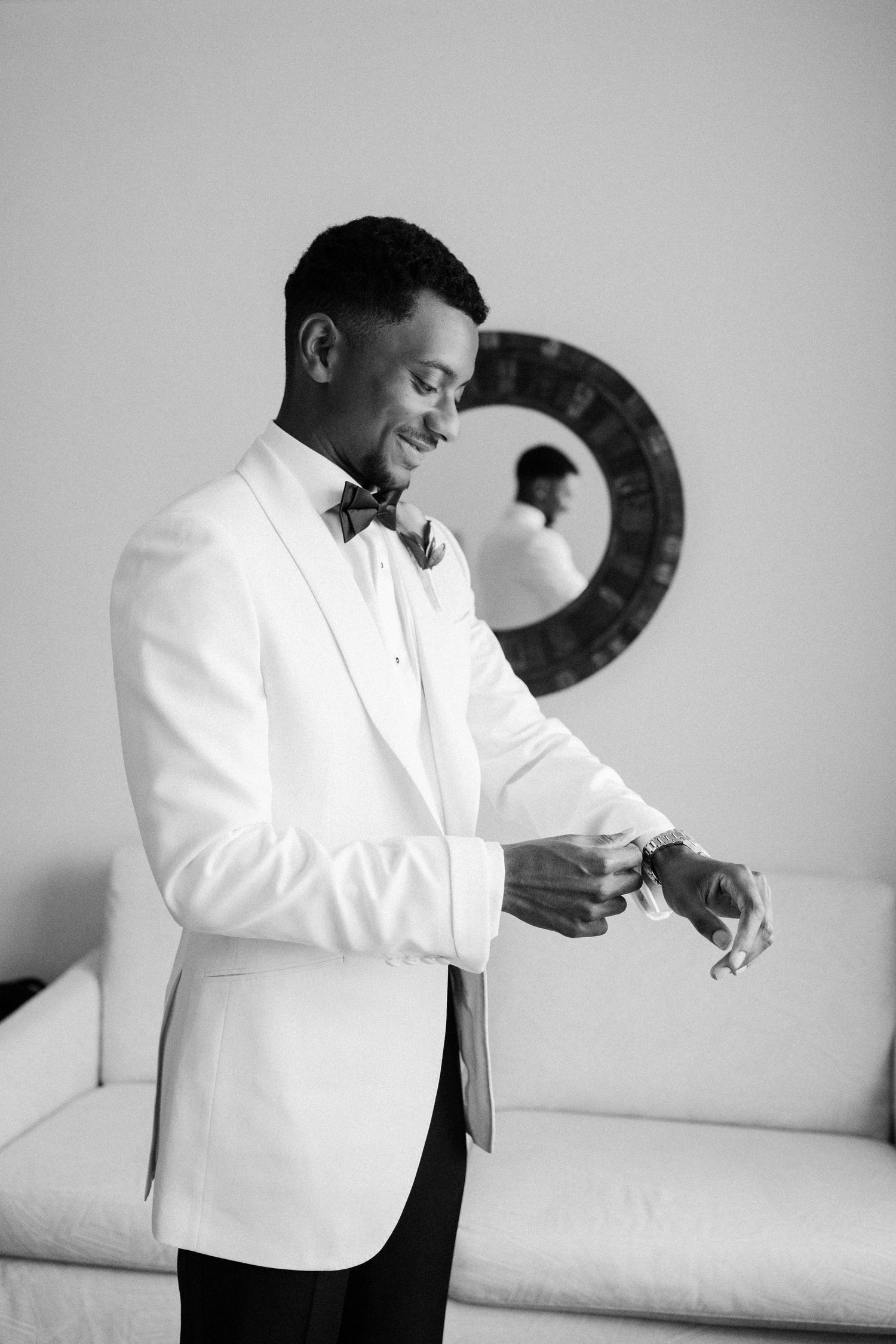 Groom in white tuxedo jacket and bow tie adjusting his watch before wedding ceremony. Barbados Destination Wedding Photographer