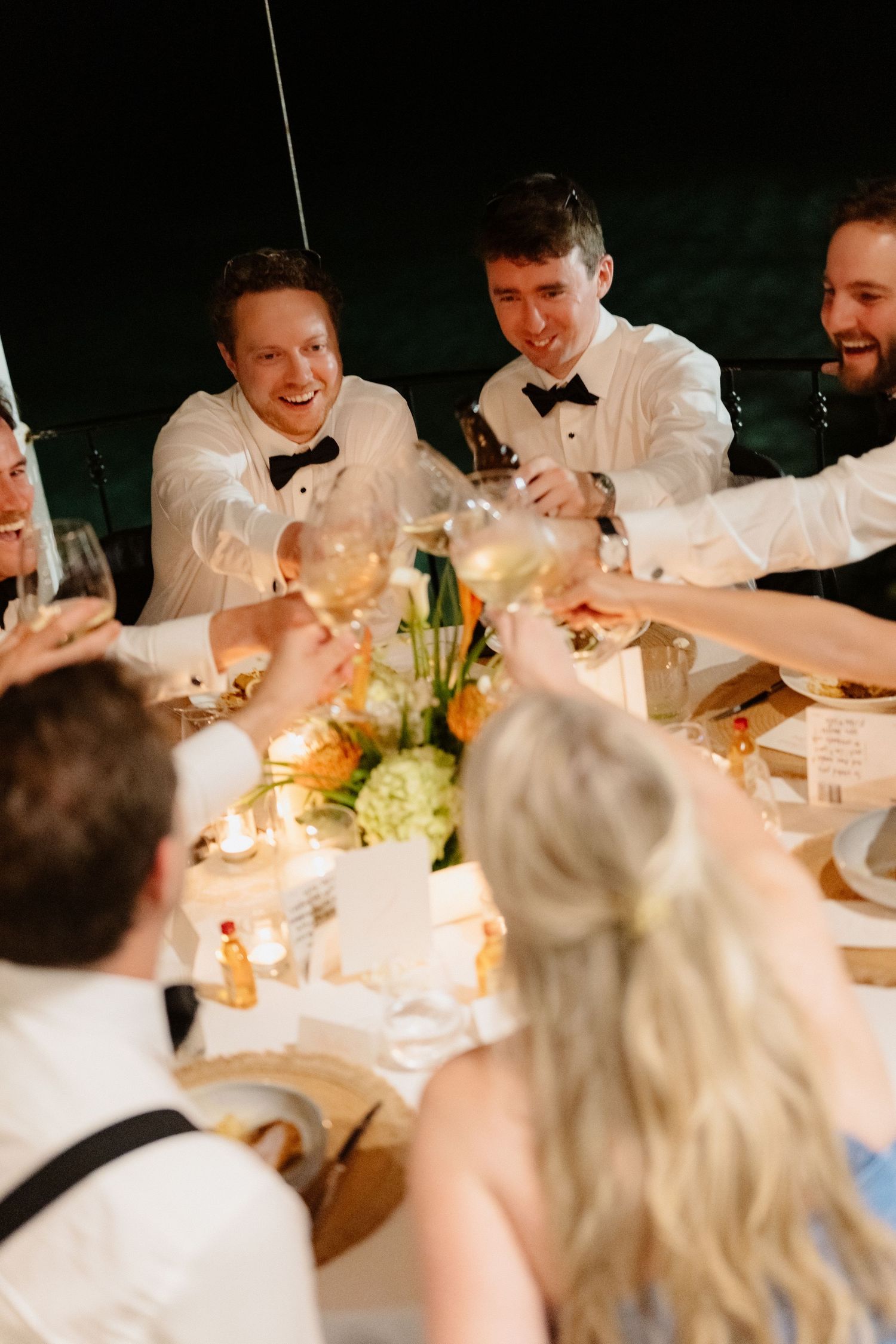 Wedding guests raising glasses of white wine in a joyful toast at an elegant reception dinner table. Barbados Destination Wedding Photograph