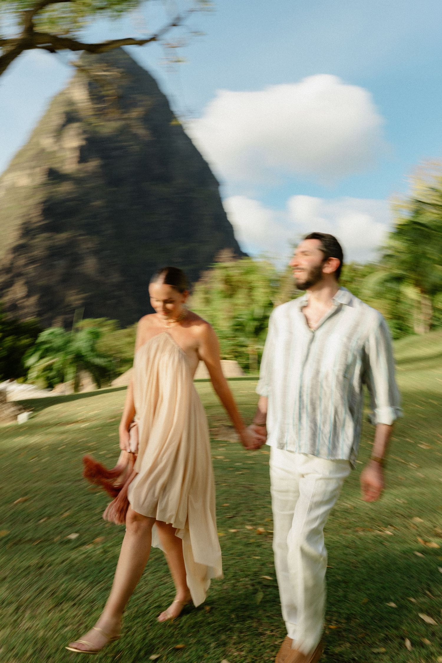 Couple holding hands walking on tropical lawn with volcanic mountain peak in background. St Lucia Wedding photographer