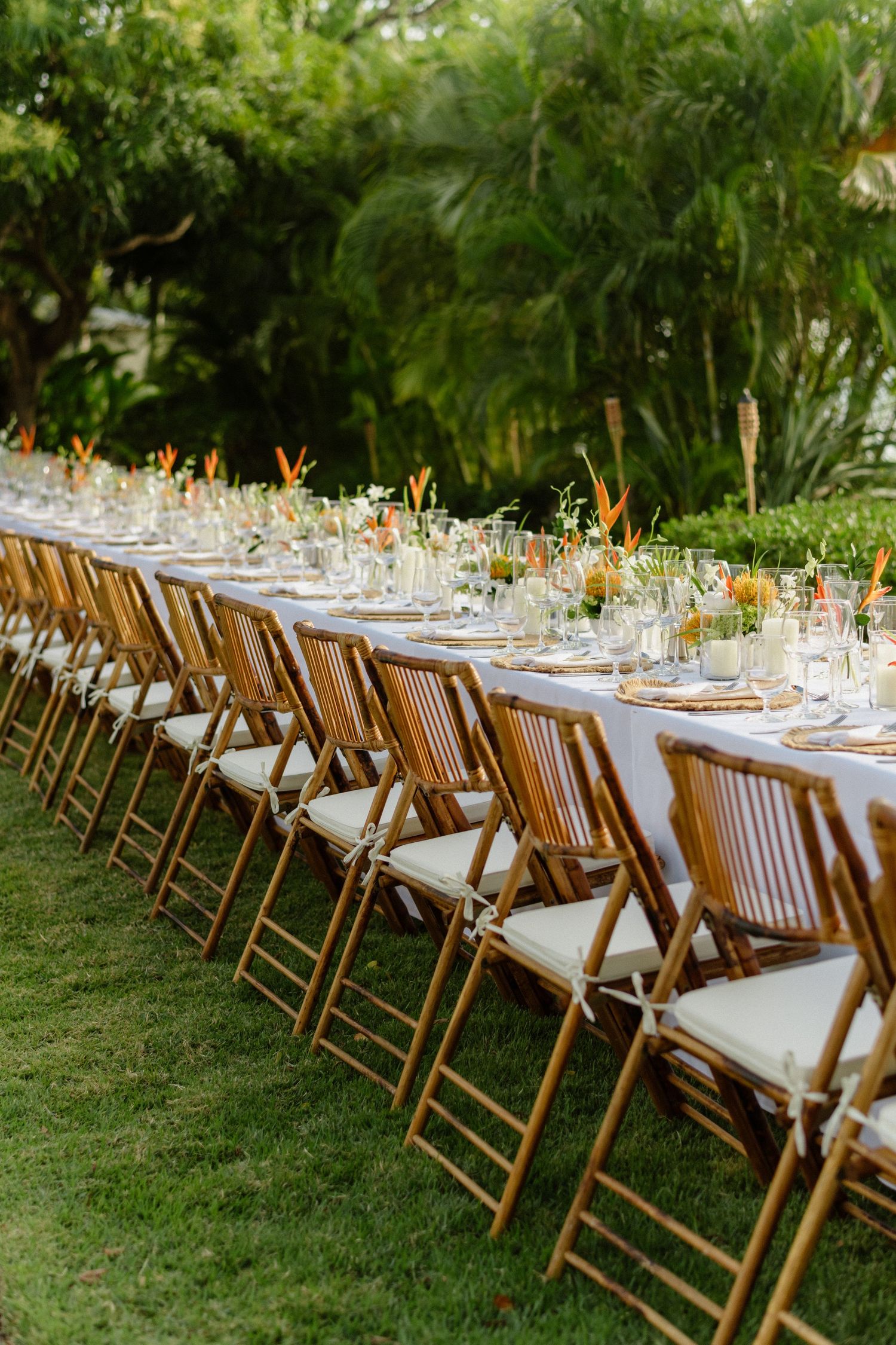 Long outdoor wedding reception table with bamboo chairs, tropical florals, and orange centerpieces. Barbados photographer