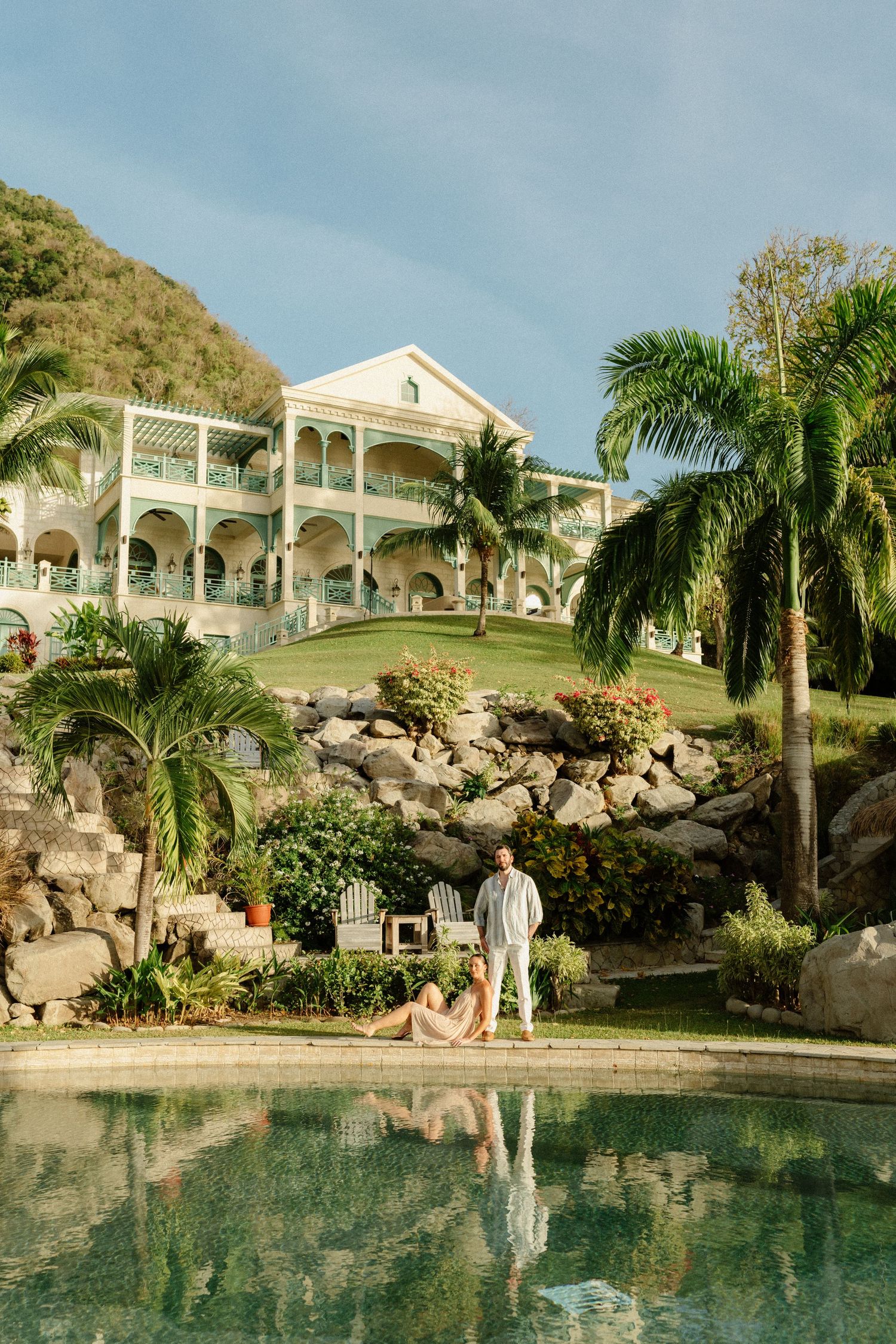 Couple relaxing by pool at luxury Caribbean resort with palm trees and colonial mansion. St Lucia Wedding photographer