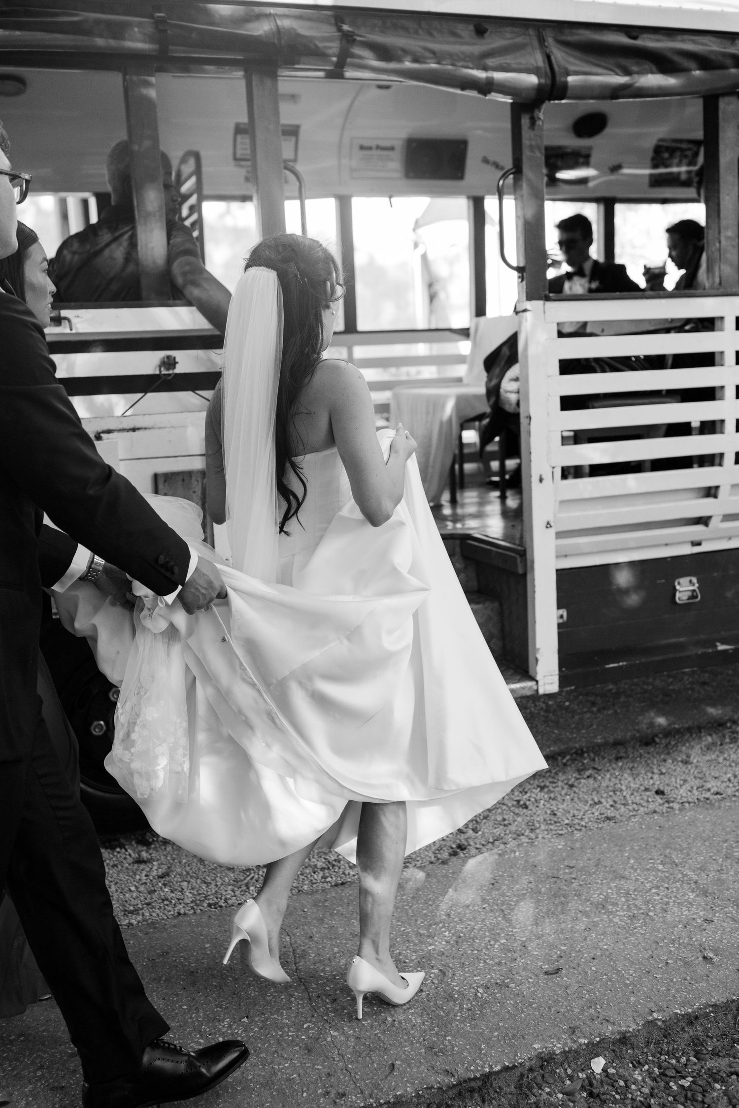 Bride in white gown and veil boards a vintage trolley assisted by groom in black and white photo. Barbados Destination Wedding Photographer