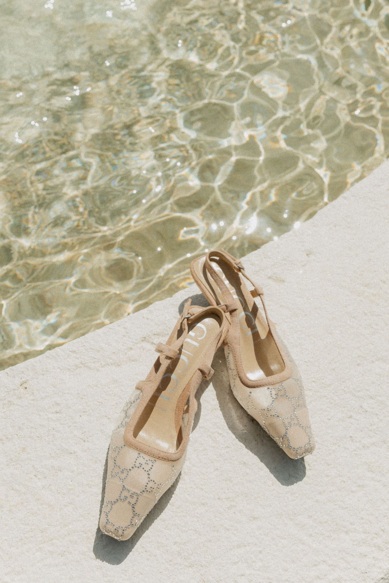 Luxury Gucci slingback heels placed beside shimmering turquoise pool water in bright sunlight. Barbados Destination Wedding Photographer