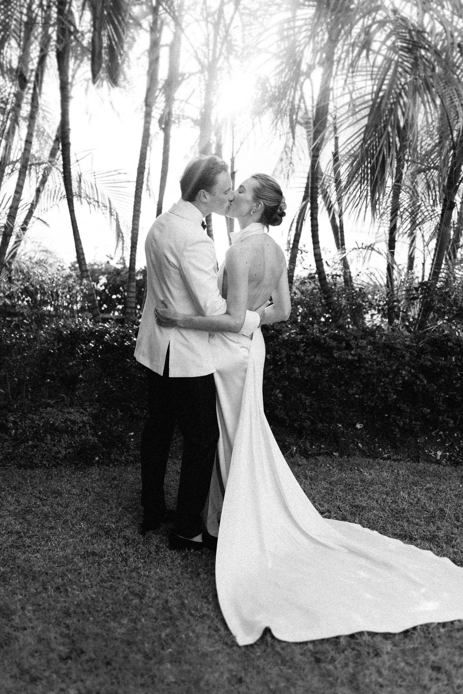 Bride and groom sharing a kiss among tropical palm trees in elegant black and white wedding photo. Barbados Destination Wedding Photographer