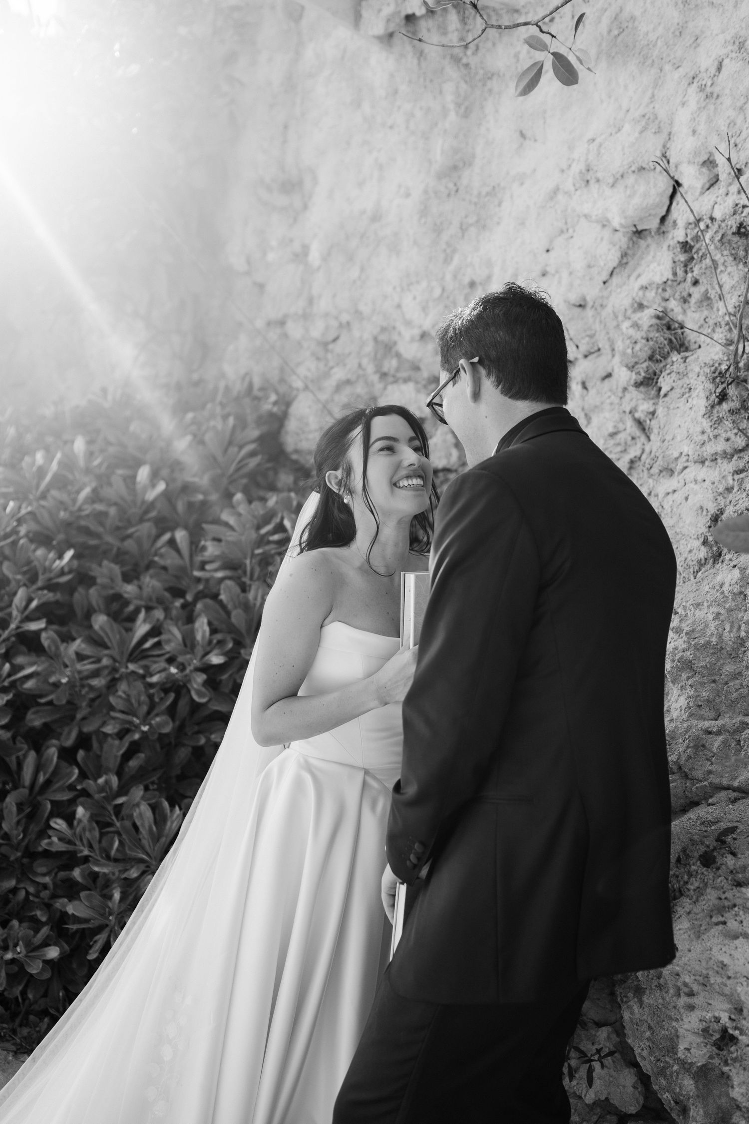 Bride and groom share an intimate moment laughing together against a rustic stone wall backdrop. Barbados Destination Wedding Photographer