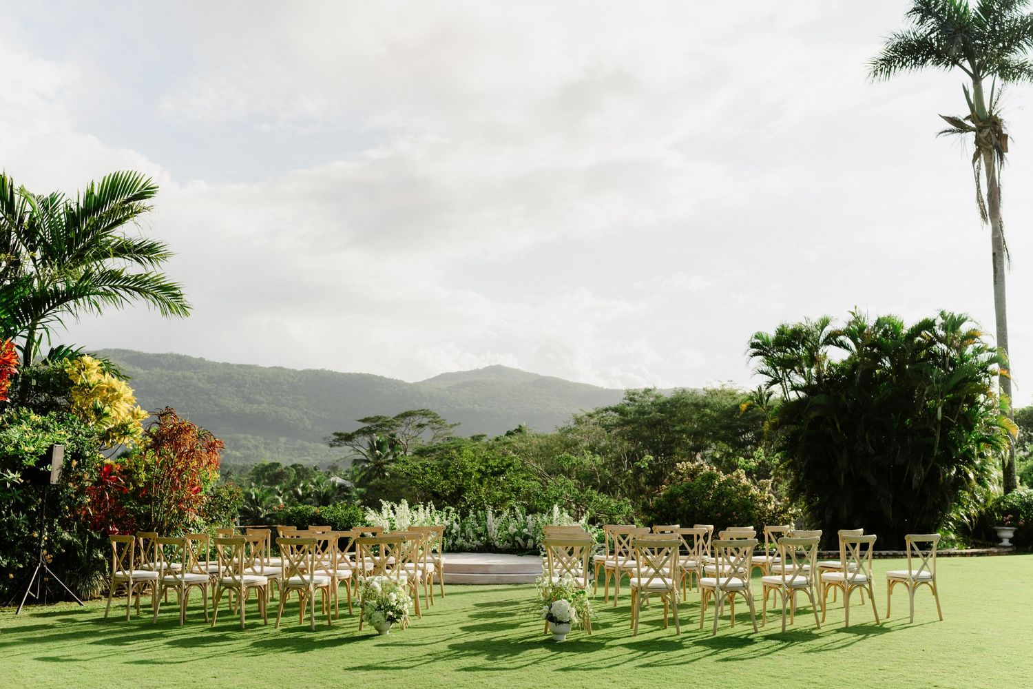 Tropical outdoor wedding ceremony setup with wooden chairs on green lawn with mountain views. Barbados Destination Wedding Photographer