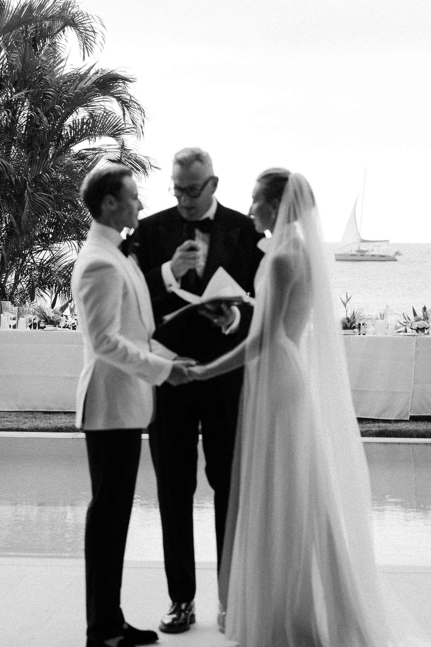 Bride and groom exchange vows with officiant at waterfront wedding ceremony, sailboat visible in background. Barbados photographer