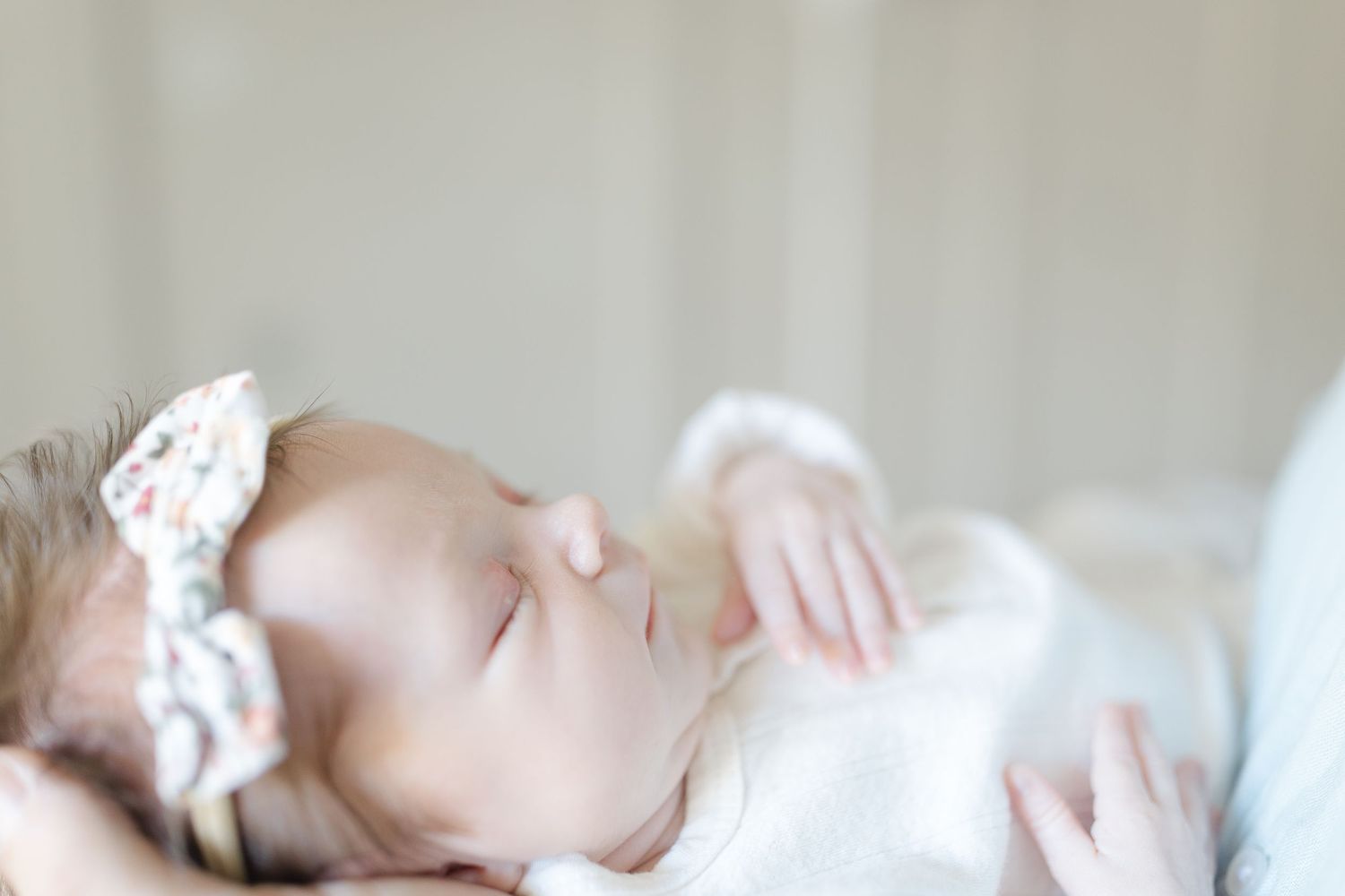 Peaceful sleeping newborn baby wearing a floral bow headband in soft natural light.  | Karina Thomson Photography Raleigh NC