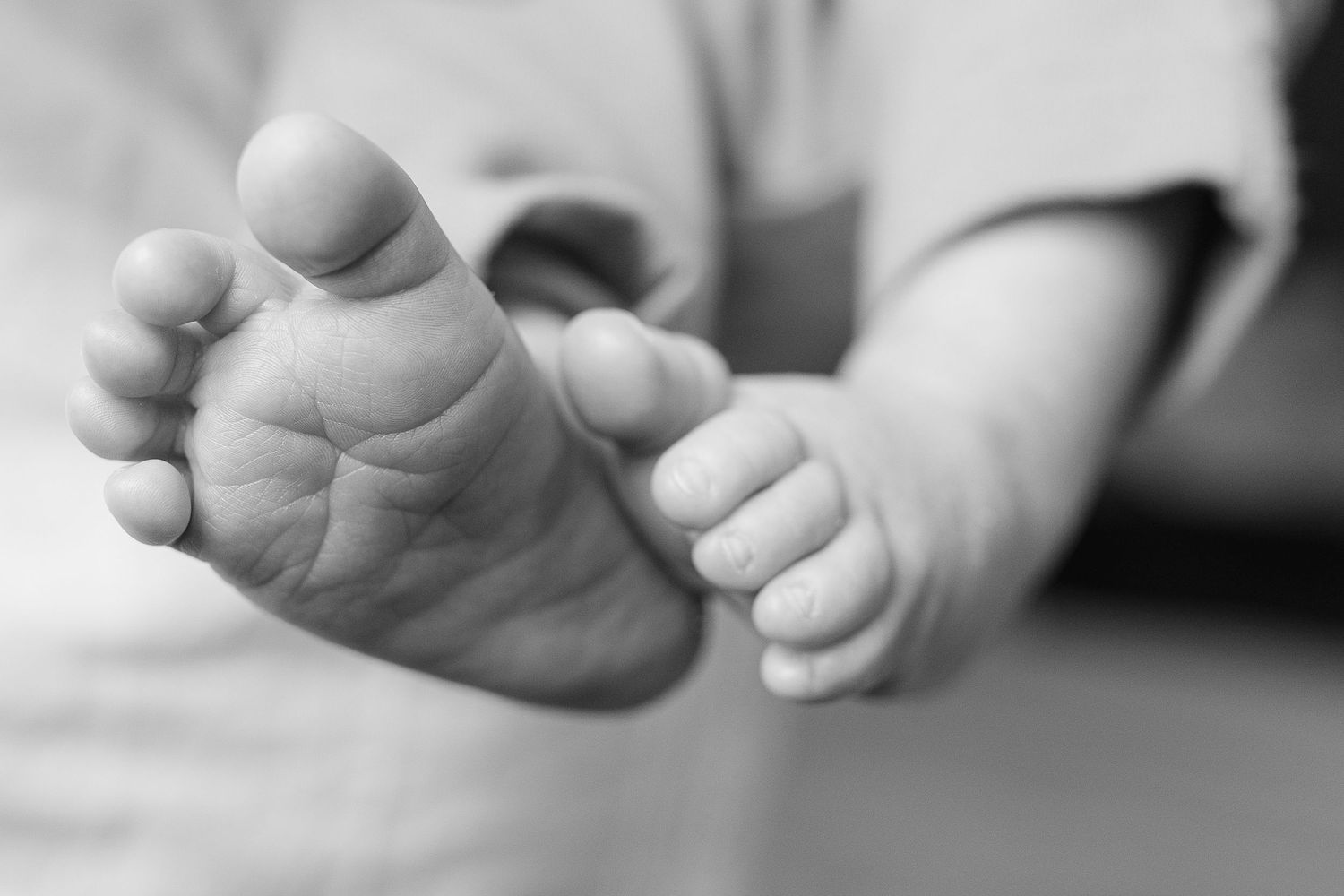 Close-up black and white photo of a newborn baby's tiny feet and hands resting gently together.