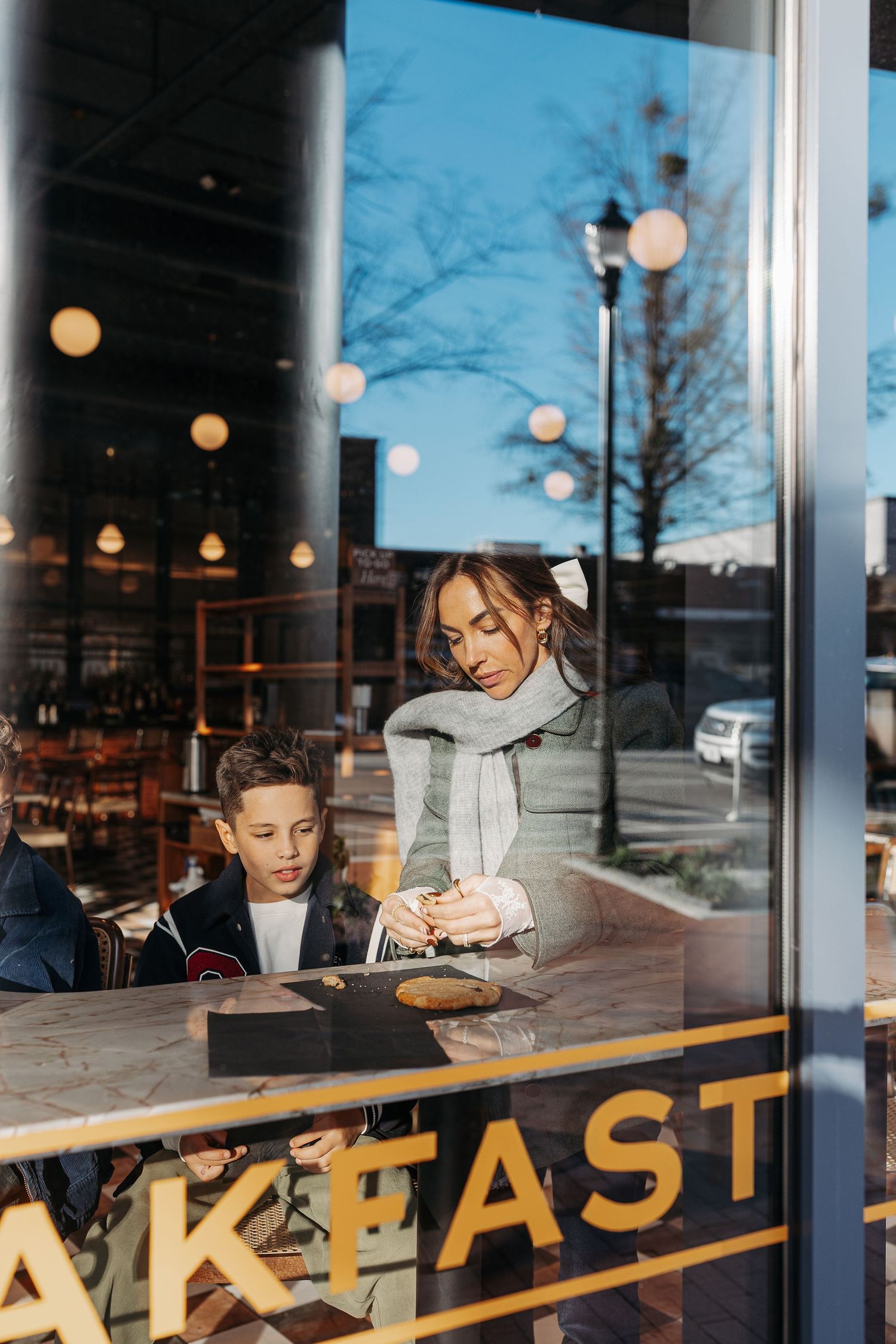 Mother and son sit together at a breakfast cafe, viewed through a window reflection.  | Karina Thomson Photography Raleigh NC