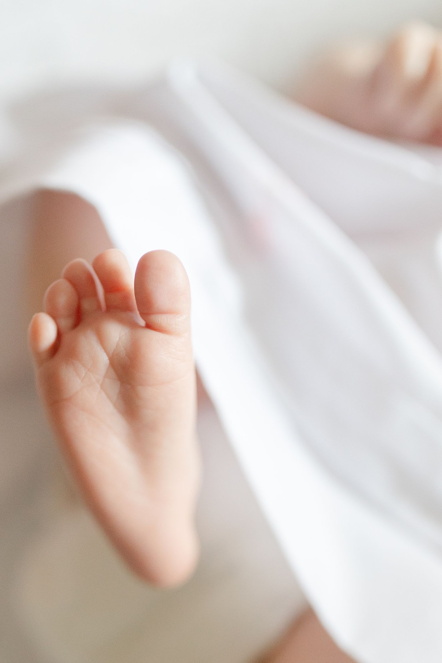 Soft focus close-up of a newborn baby foot peeking out from a white swaddle blanket.  | Karina Thomson Photography Raleigh NC