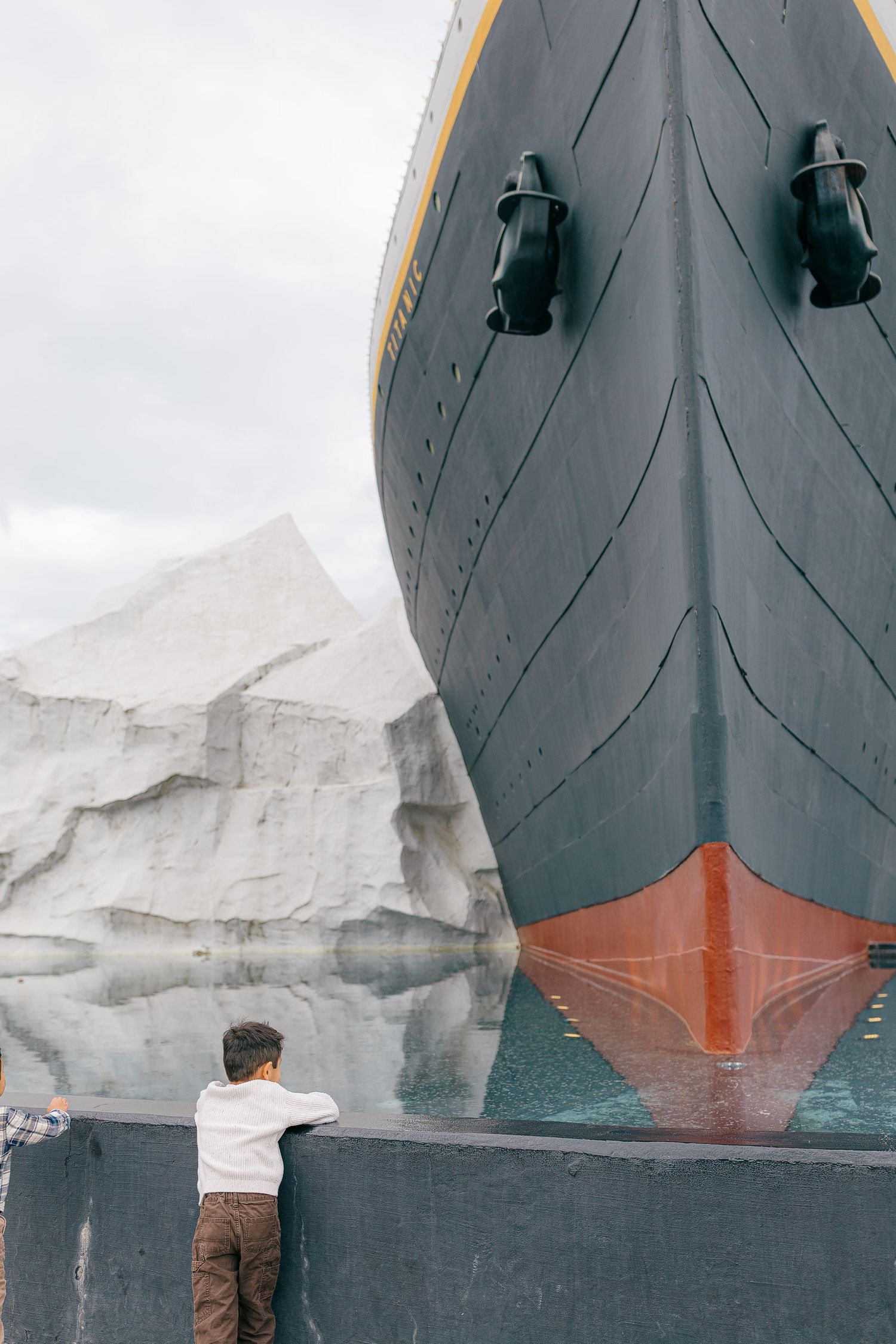 Young boy looking up at massive ship bow beside large iceberg display at museum exhibit.  | Karina Thomson Photography Raleigh NC
