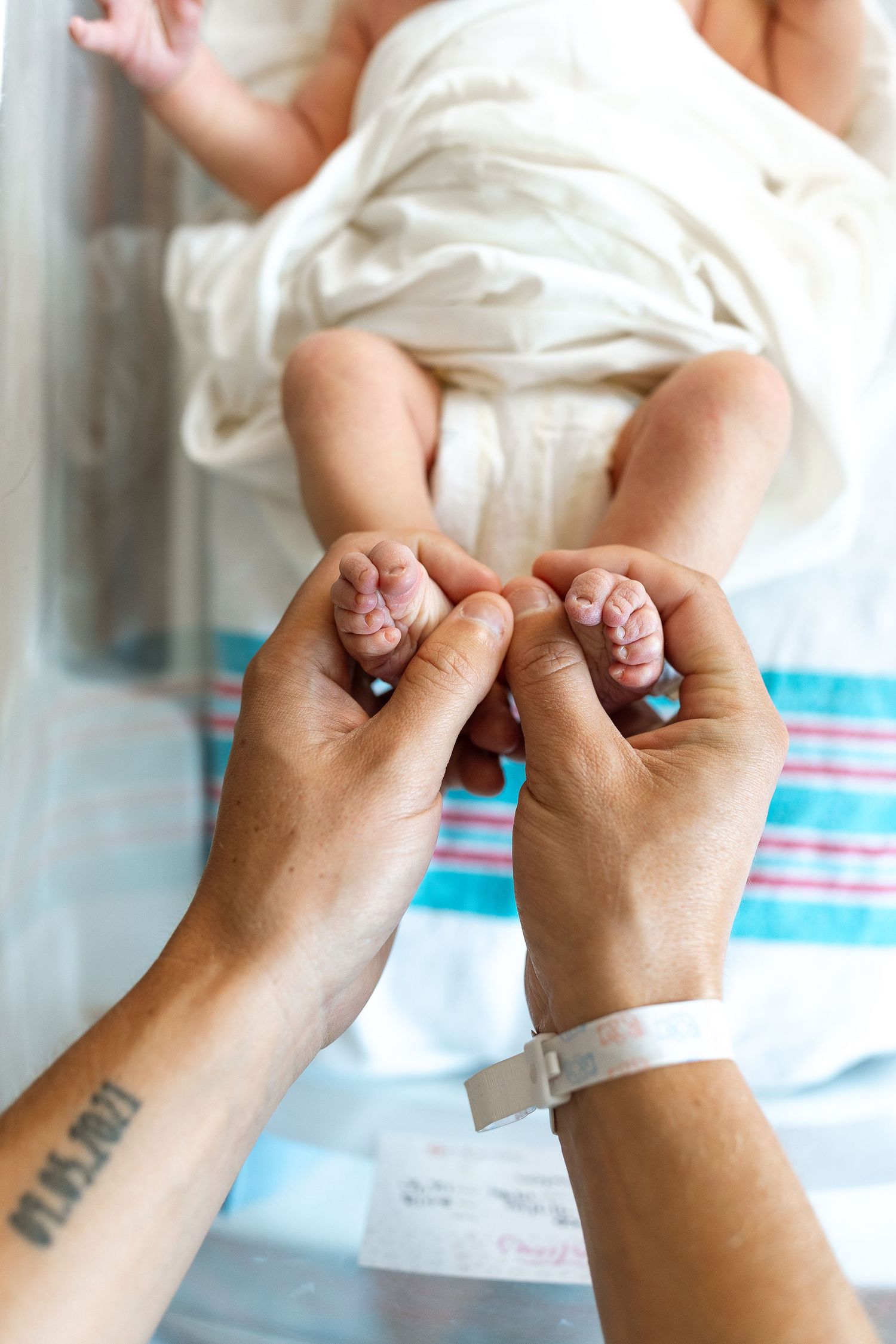Parent holding newborn baby's tiny feet in hospital, with ID bracelet visible on wrist.