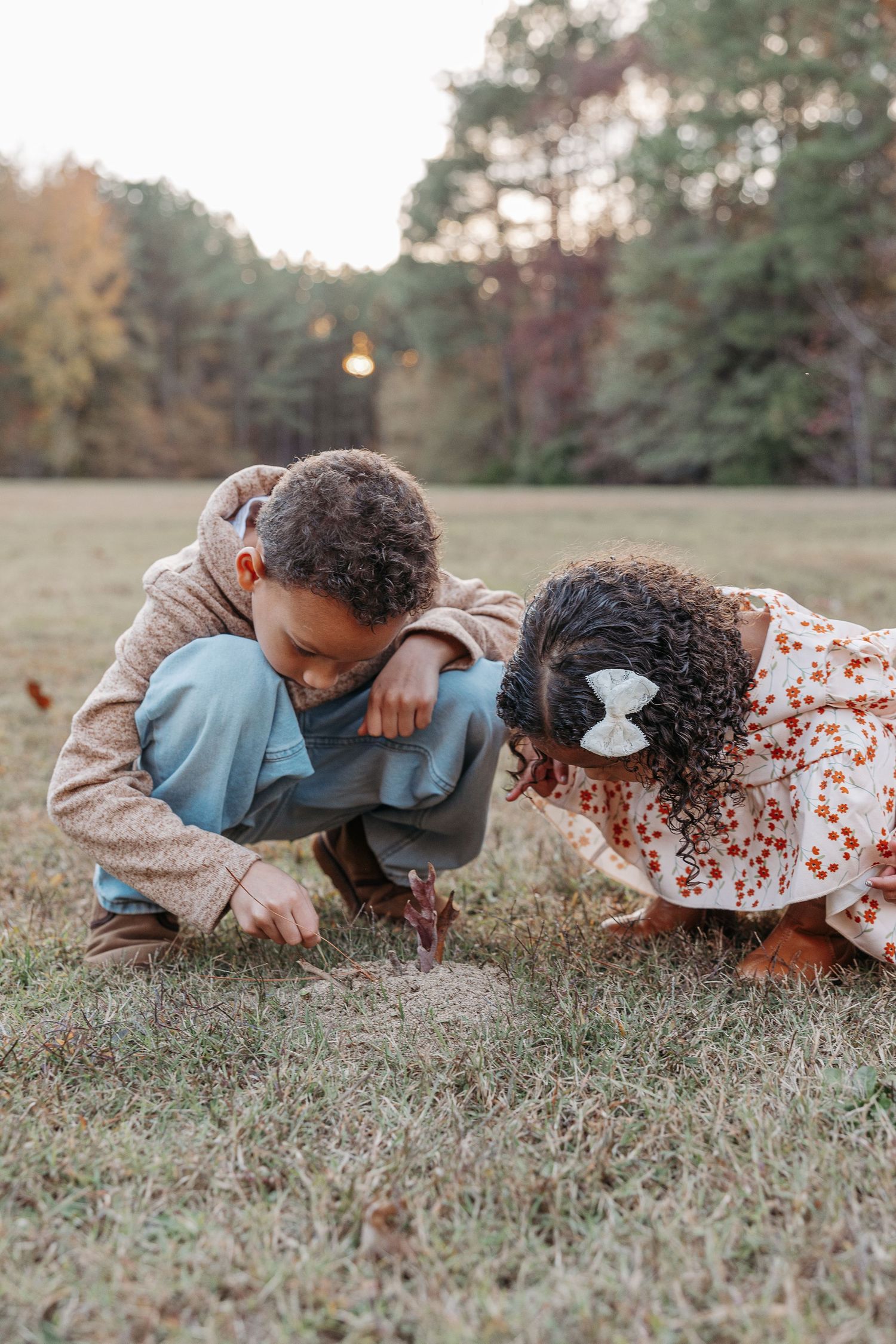 Two young children crouching on grass examining something on ground in autumn park.  | Karina Thomson Photography Raleigh NC