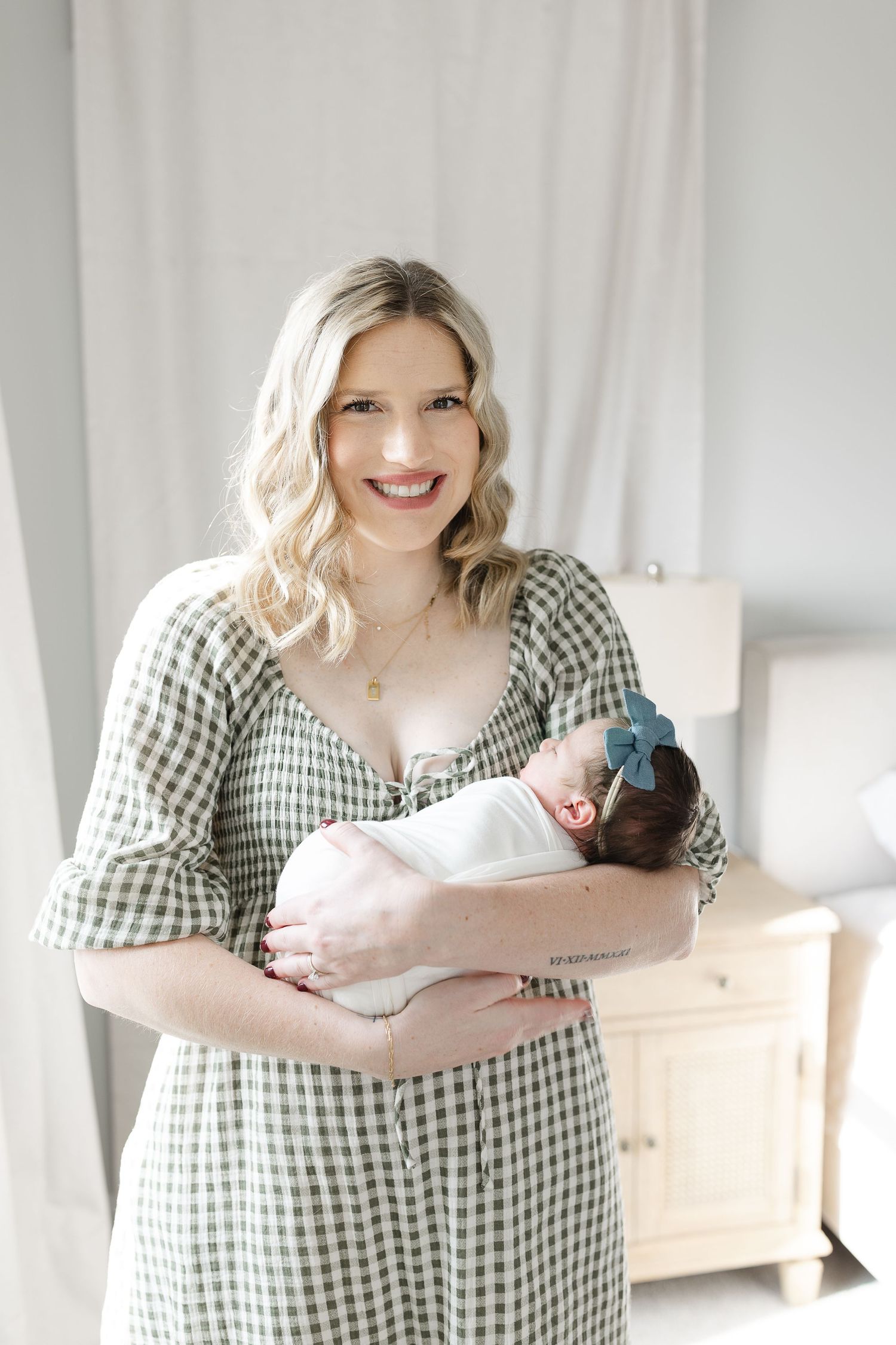 Smiling blonde mother in green gingham dress holding her swaddled newborn baby.  | Karina Thomson Photography Raleigh NC