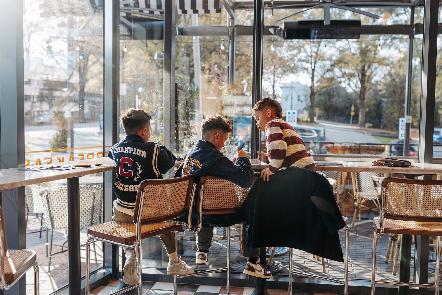 Three young people sit together at a sunlit cafe, chatting and looking at a phone.  | Karina Thomson Photography Raleigh NC