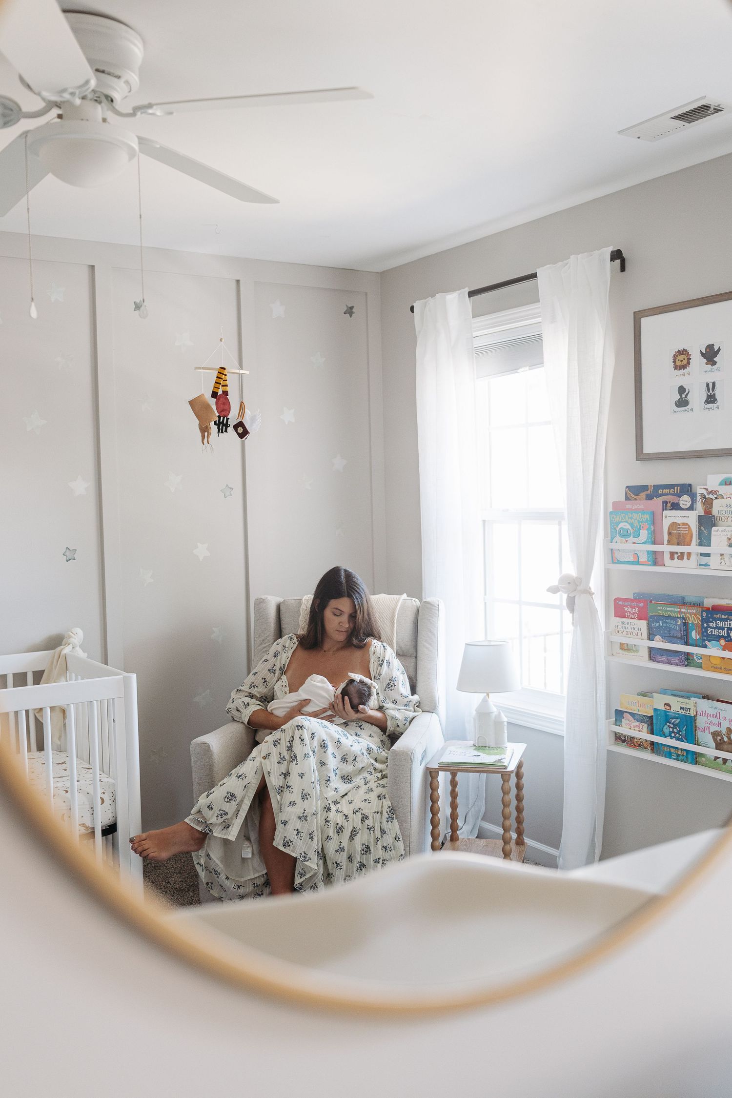 Mother nurses newborn baby in a nursery glider chair, reflected in a round mirror.  | Karina Thomson Photography Raleigh NC