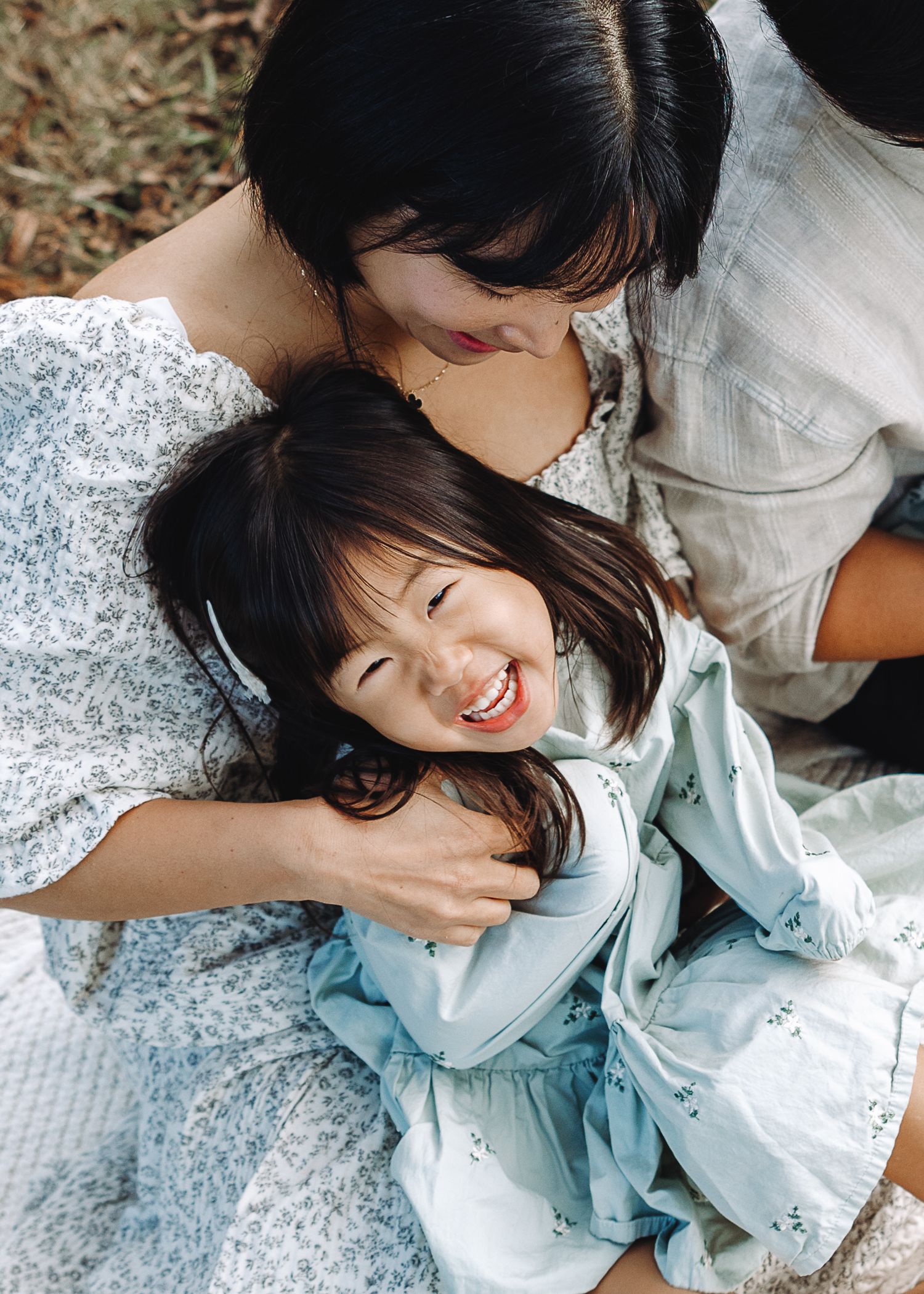 Mother and child share a joyful embrace outdoors, laughing together on the ground. | Karina Thomson Photography Raleigh NC