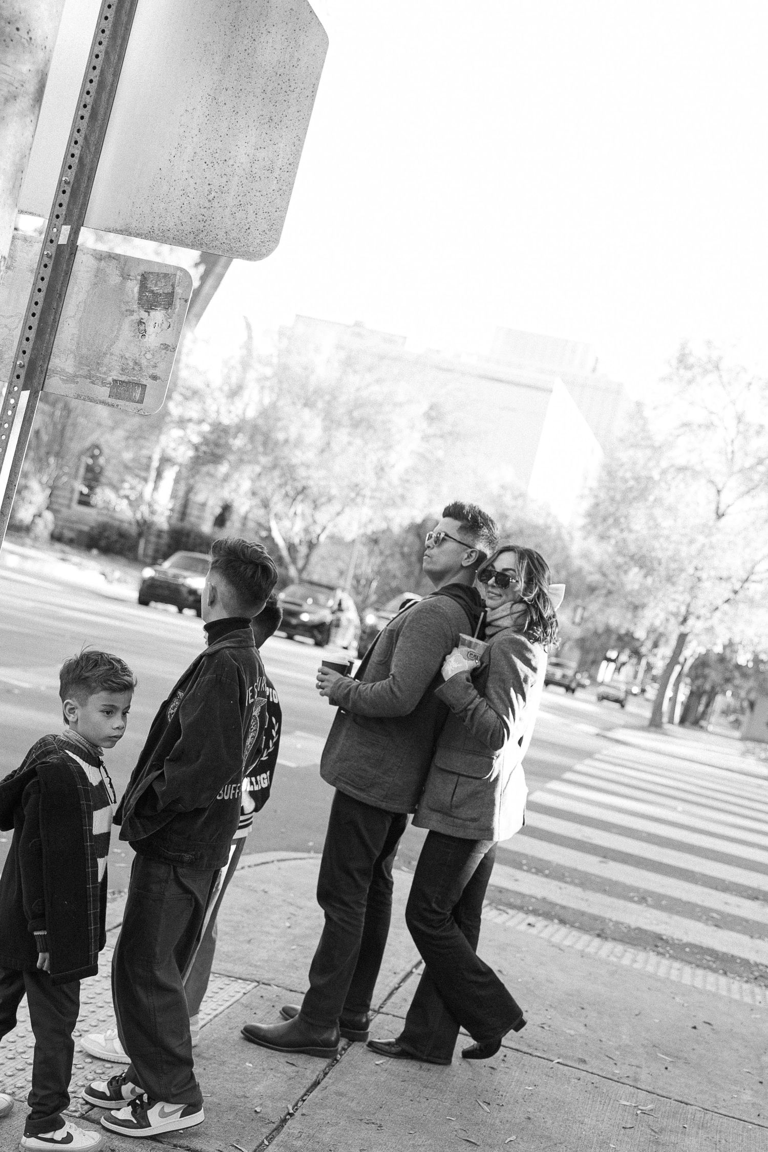 Black and white urban family photo with couple embracing and two boys standing on city sidewalk.  | Karina Thomson Photography Raleigh NC