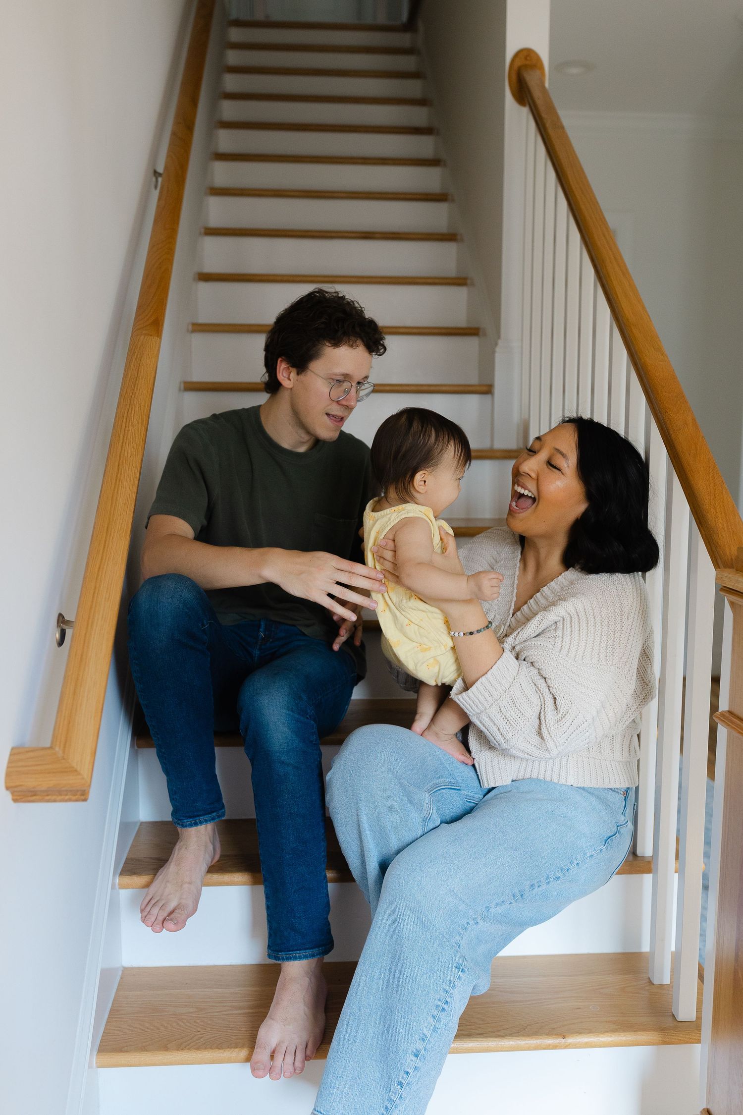 Happy family with baby sitting on wooden staircase at home, parents smiling and laughing together.  | Karina Thomson Photography Raleigh NC