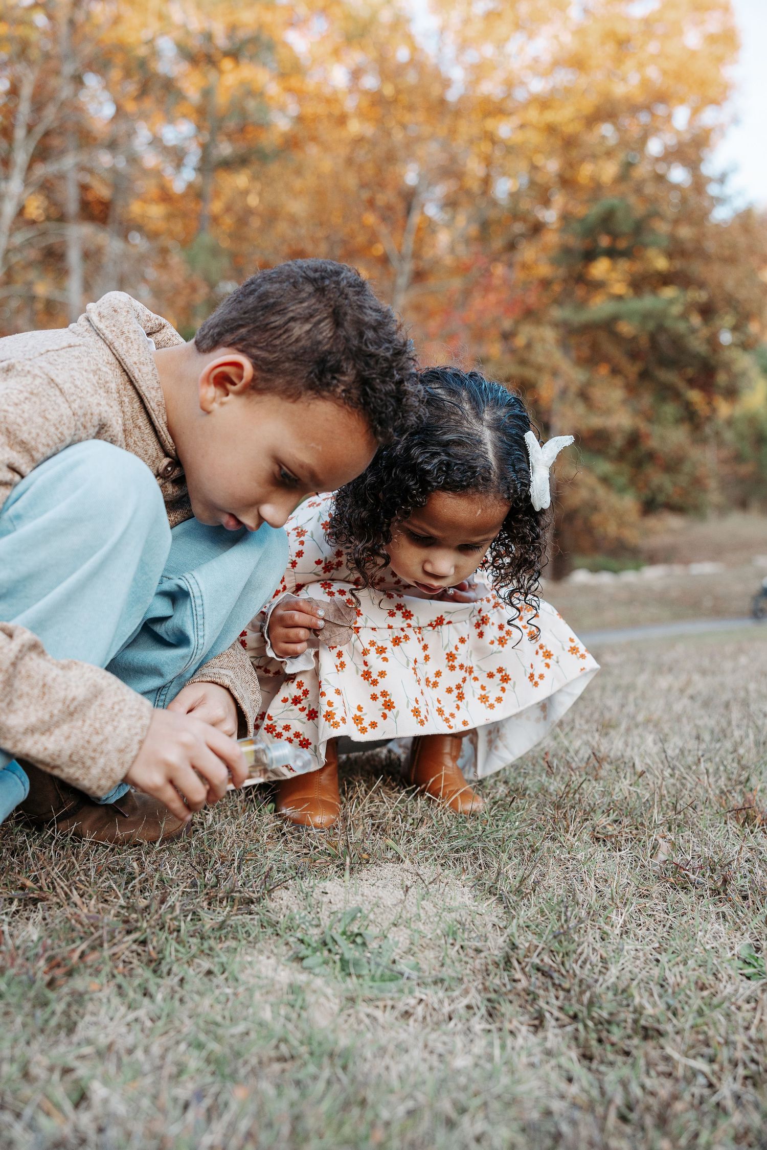 Two young children crouch in autumn grass, curiously examining something on the ground outdoors.  | Karina Thomson Photography Raleigh NC