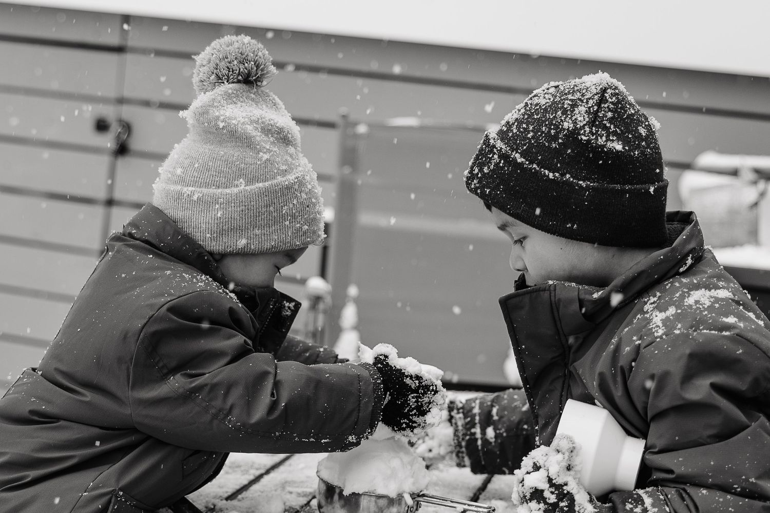 Two children in winter hats playing together in falling snow in black and white photo.  | Karina Thomson Photography Raleigh NC