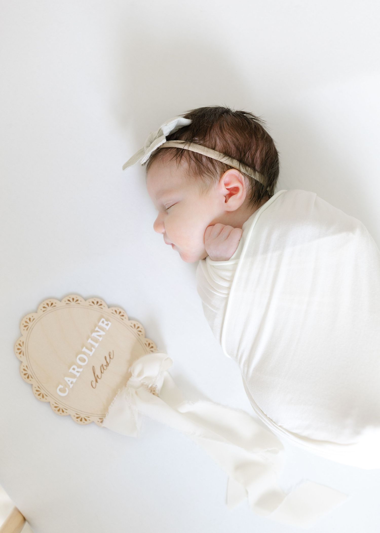 Sleeping newborn baby girl named Caroline Chase swaddled in white, holding a name sign.  | Karina Thomson Photography Raleigh NC