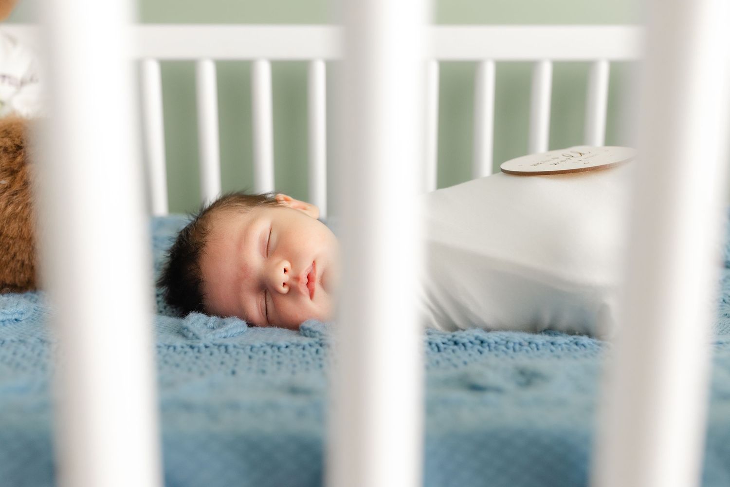 Peaceful newborn baby sleeping soundly in a white crib on a soft blue blanket.