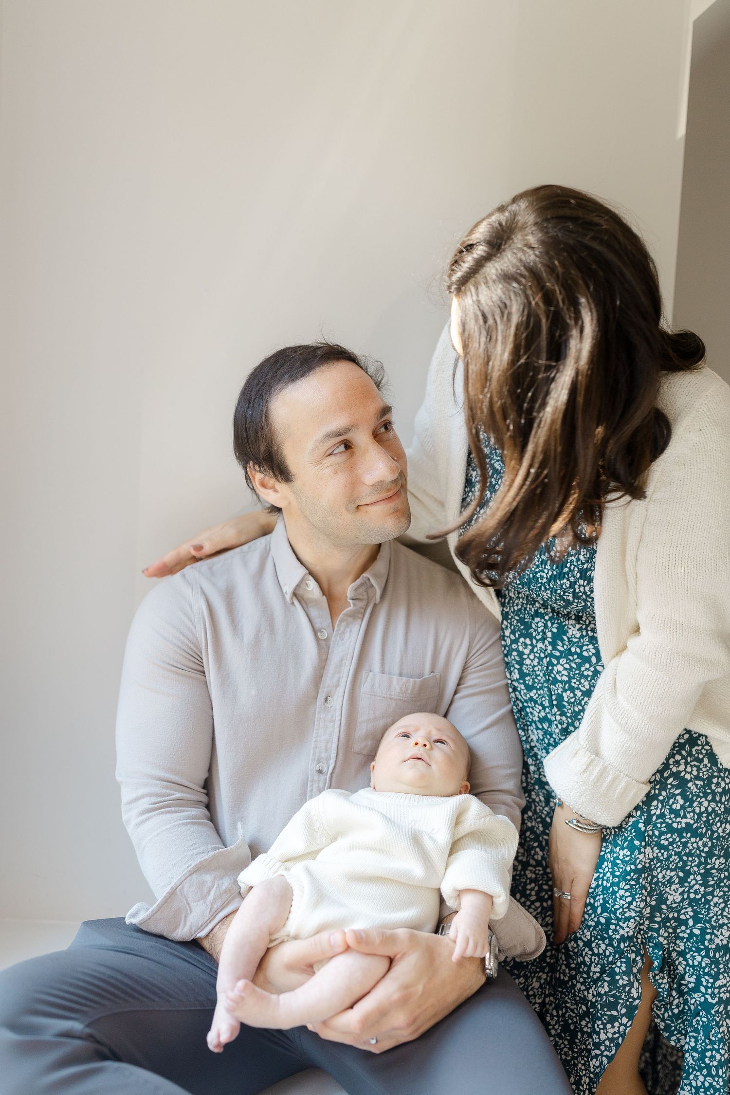 New parents sharing a loving glance while father holds their newborn baby in a bright room.  | Karina Thomson Photography Raleigh NC