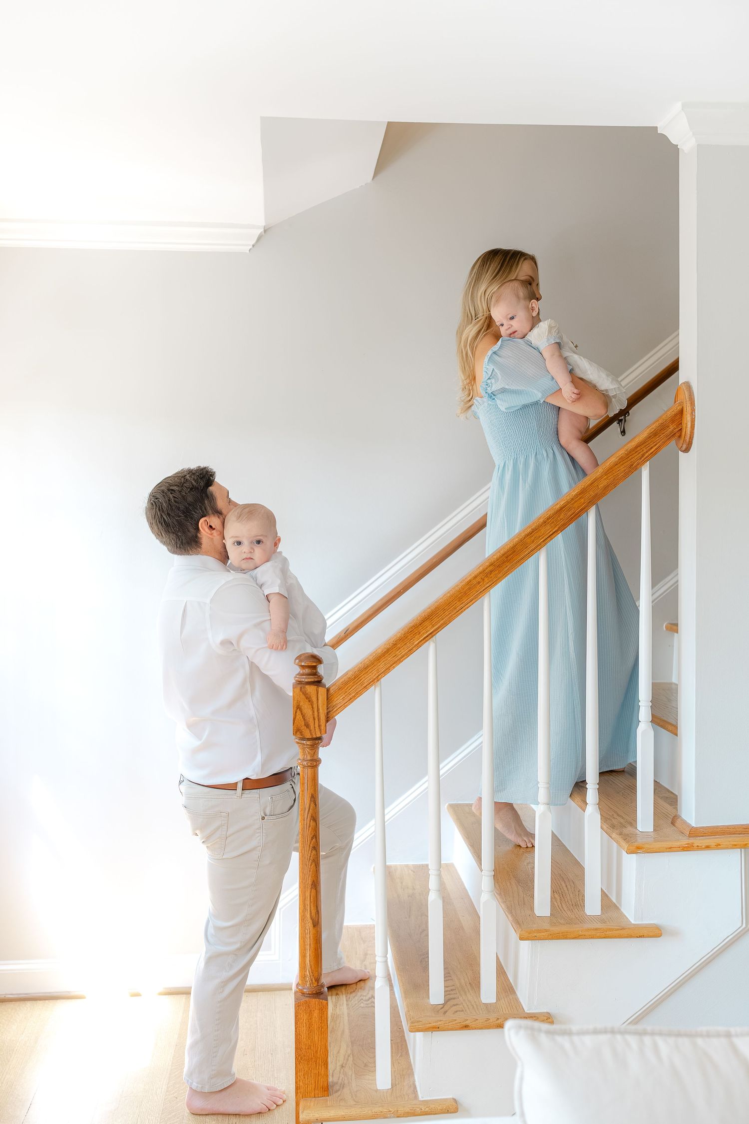 A young family with two babies on a wooden staircase, father at bottom, mother in blue dress above.