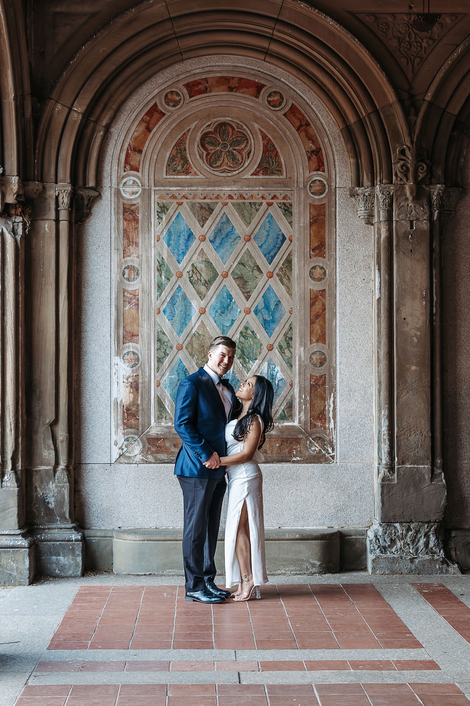 Couple in formal attire embracing romantically under ornate arch at Bethesda Terrace Central Park. | Karina Thomson Photography Raleigh NC