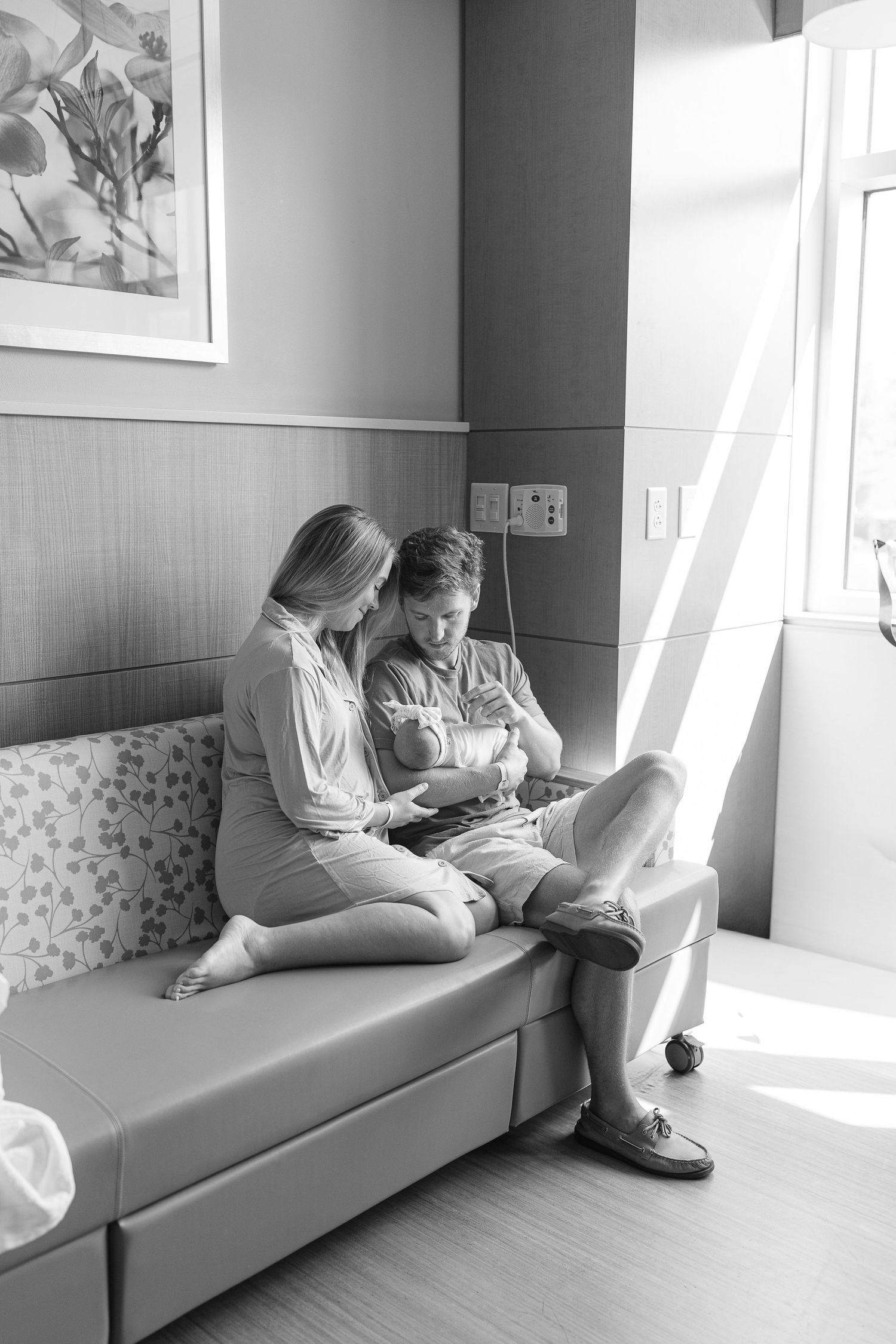 Black and white photo of a couple sitting on a hospital bed, tenderly holding their newborn baby.