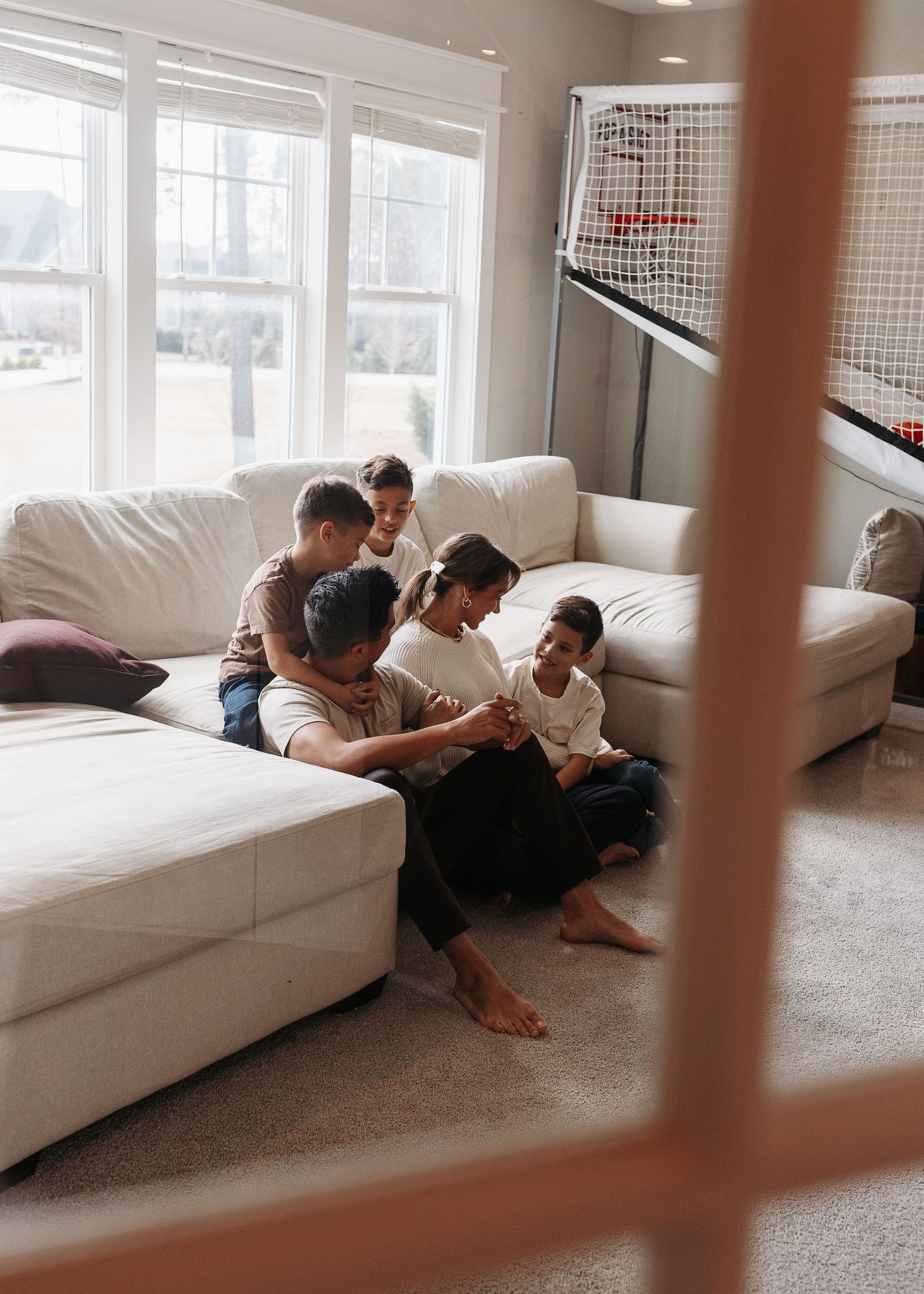 A happy family of four sits together on a white couch in a bright living room.  | Karina Thomson Photography Raleigh NC