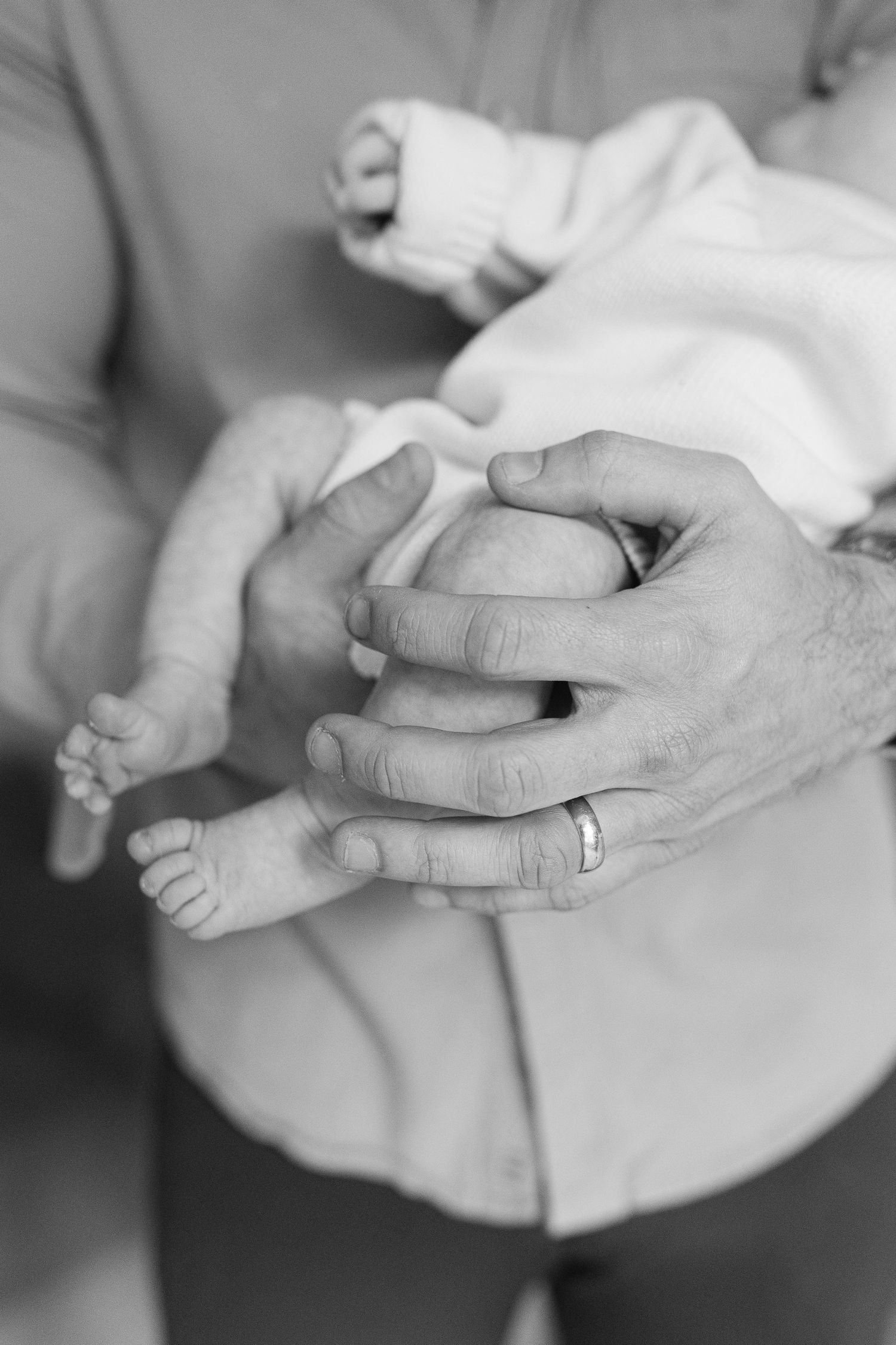 Black and white photo of a father holding his newborn baby, wedding ring visible. | Karina Thomson Photography Raleigh NC