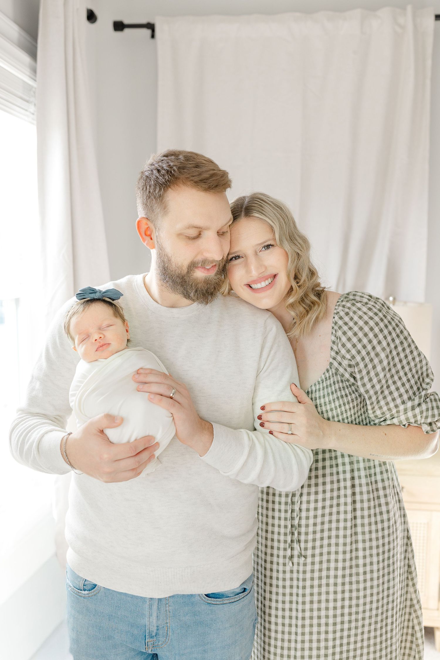 Happy couple holding their swaddled newborn baby girl in a bright white room.  | Karina Thomson Photography Raleigh NC