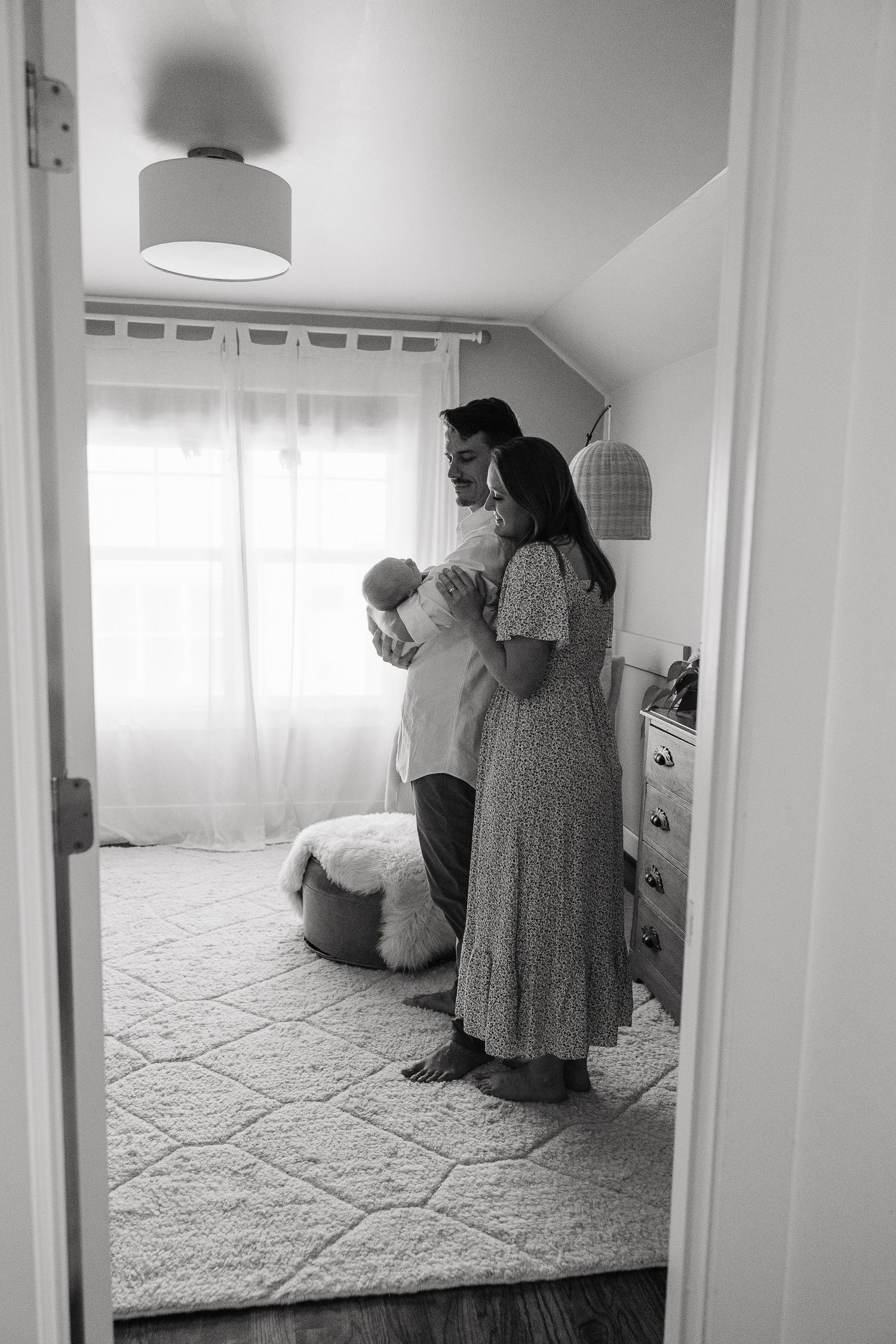 Black and white image of new parents standing together holding  their newborn in a nursery.  | Karina Thomson Photography Raleigh NC