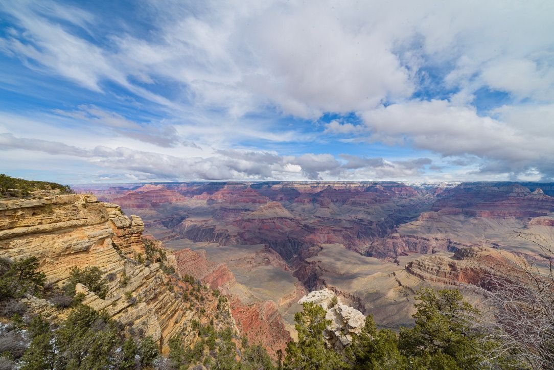 Panoramic view of the Grand Canyon with layered red rock formations under a partly cloudy blue sky.