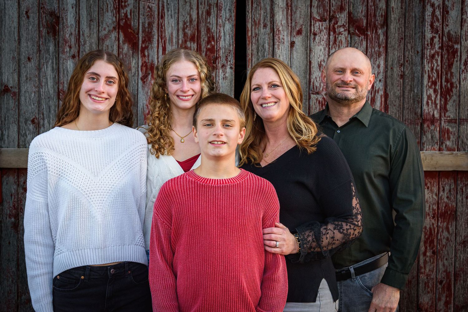 Family of five smiling together in front of a rustic red barn door. Polk County, NE
