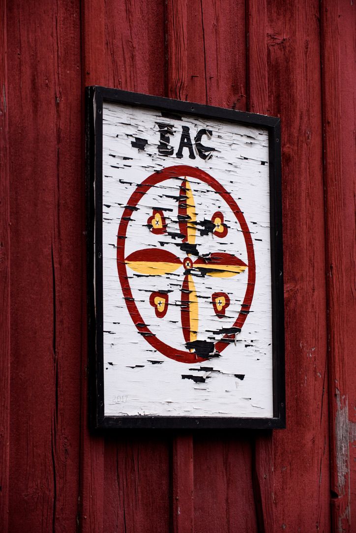 Weathered EAC sign with cross emblem mounted on a red wooden barn wall.