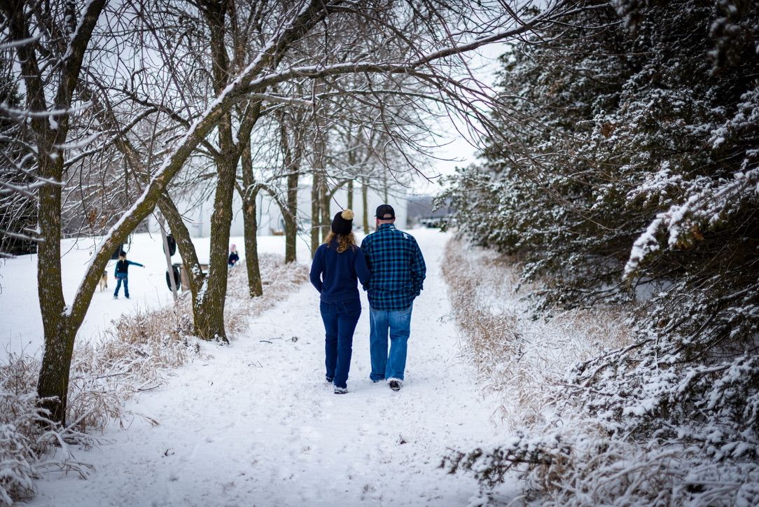 Couple walking hand-in-hand on a snowy winter path lined with snow-covered trees.