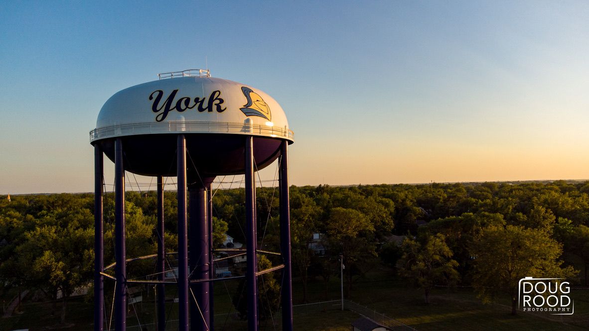 Aerial drone photo of York water tower at golden hour sunset with trees and town visible below in Nebraska.