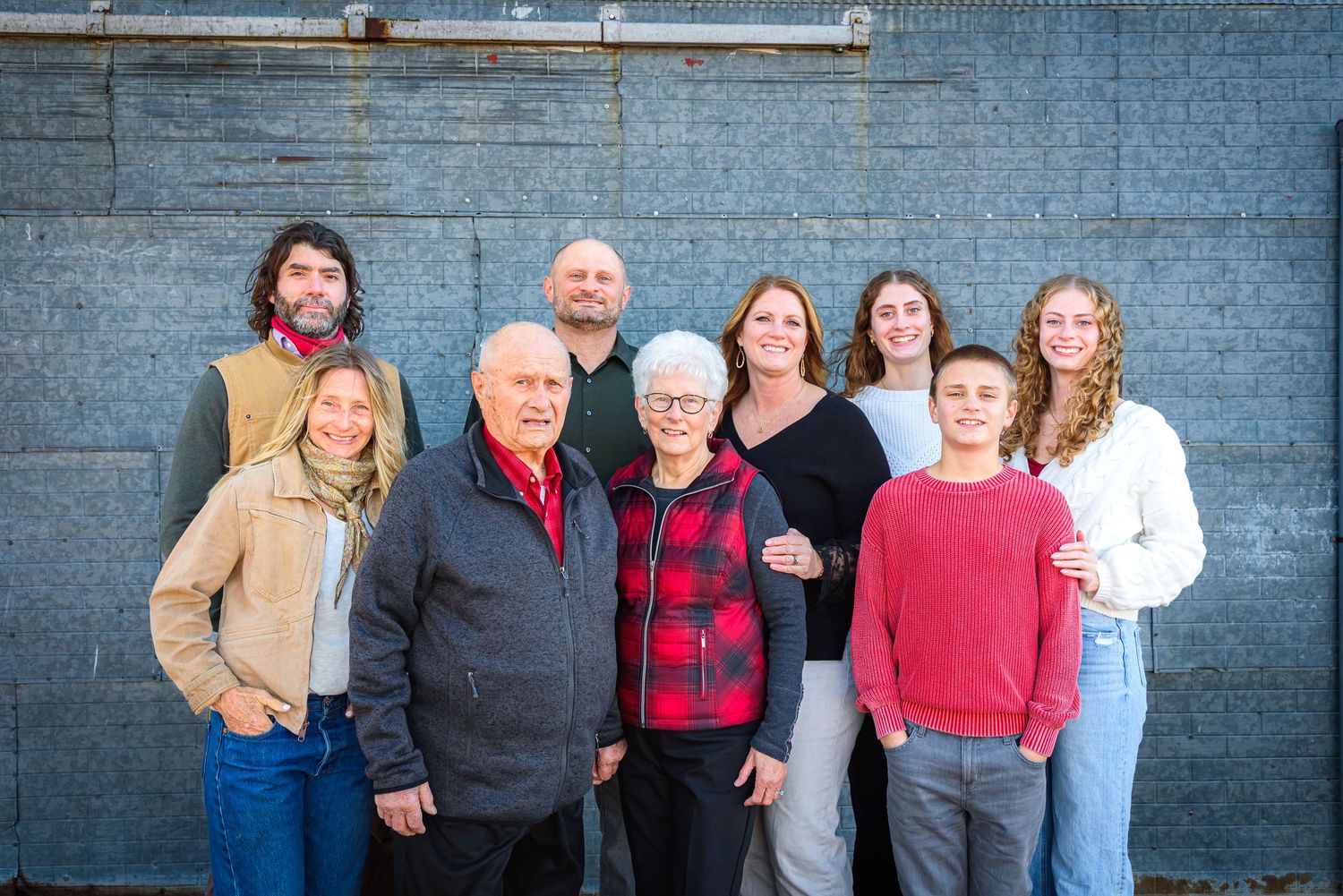 Extended family of nine smiling together against a gray brick wall outdoors. Polk County, NE