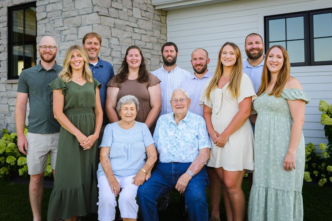 Multi-generational family portrait of 11 people posing outdoors in front of a modern home.