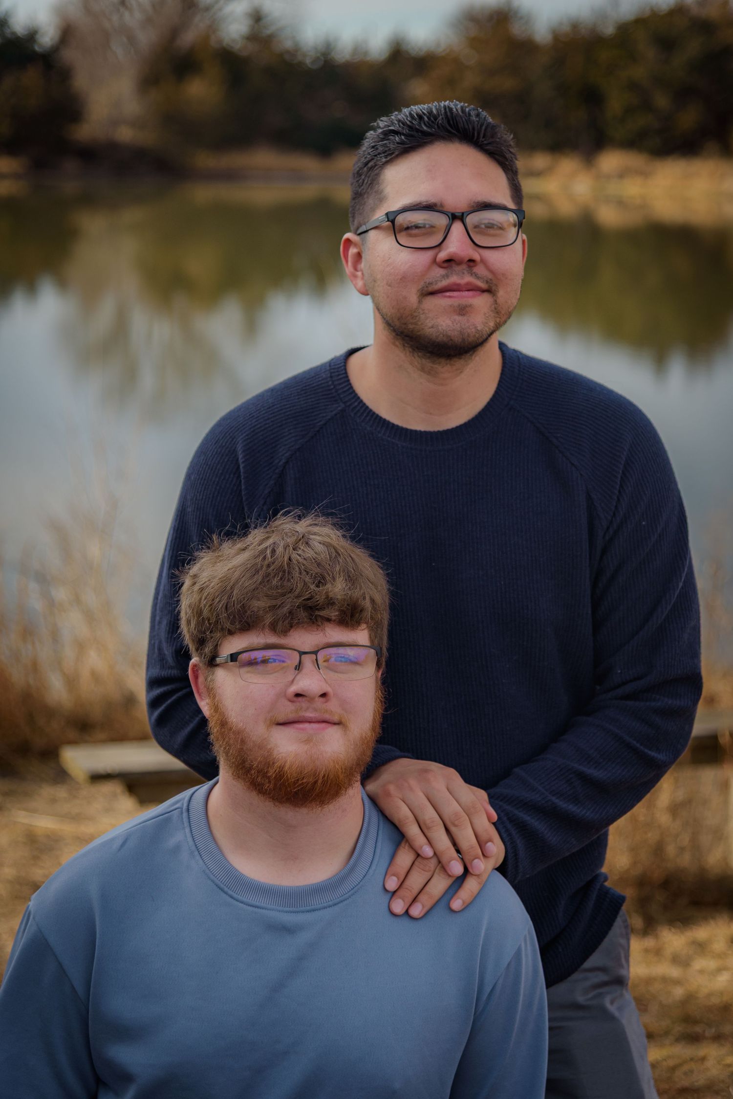 Two young men posing together near a lake, one standing behind the other outdoors. York, NE