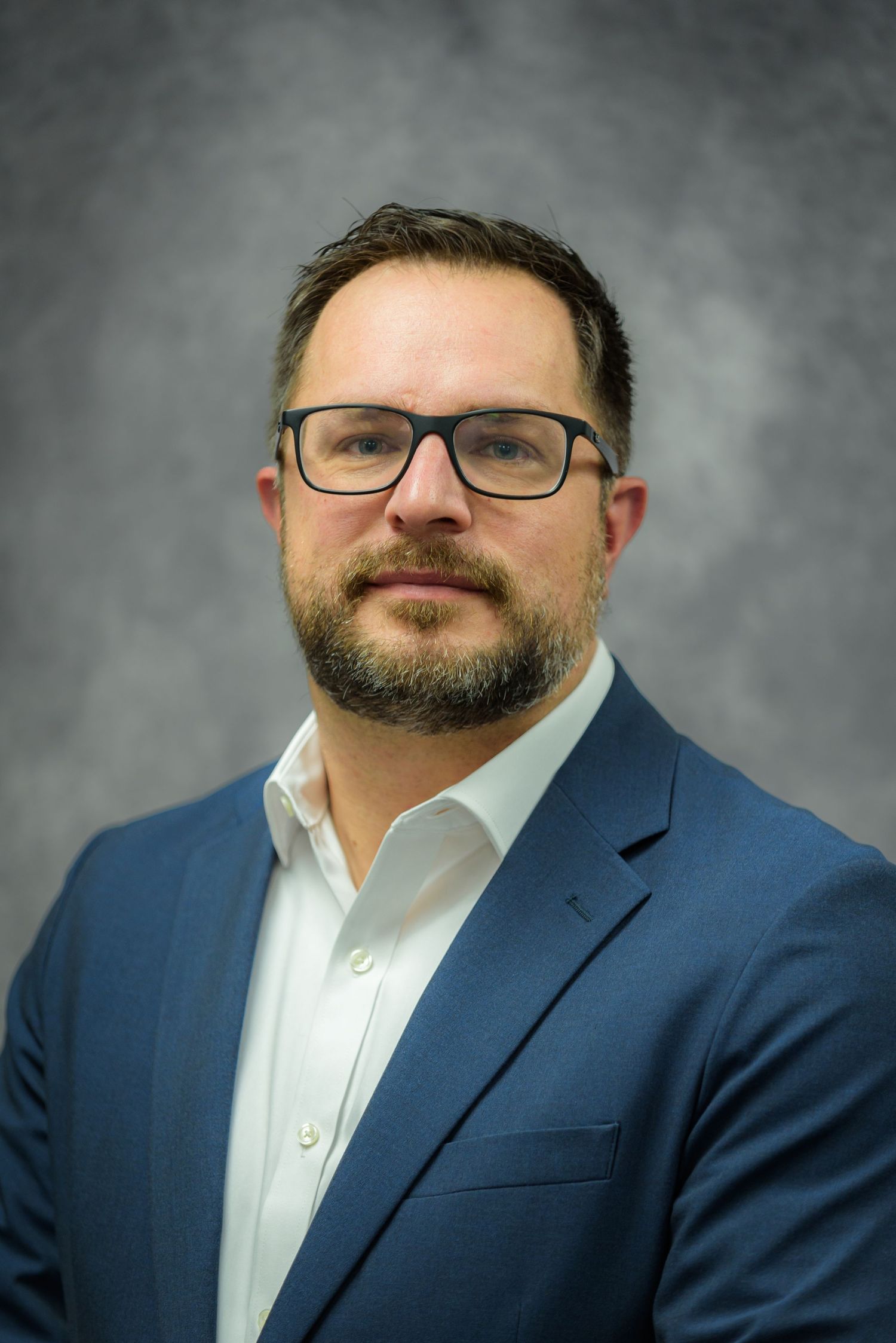 Professional headshot of a bearded man wearing glasses and a blue blazer over a white shirt.
