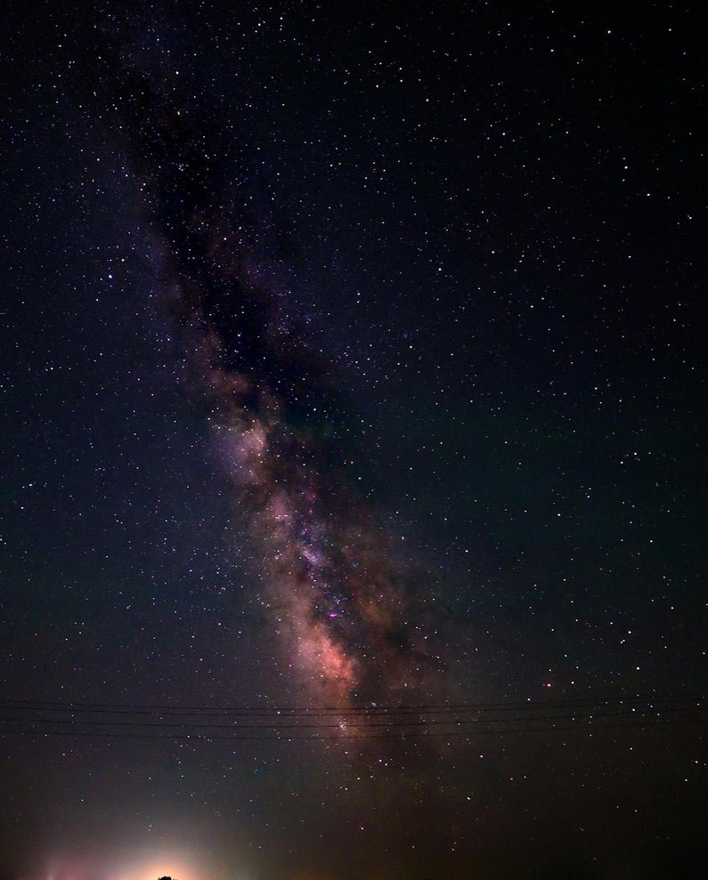 Stunning Milky Way galaxy stretching across a dark night sky with vibrant purple and pink hues above a flat horizon.