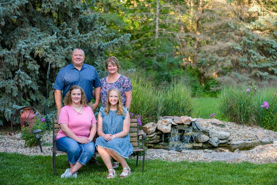 Family of four poses in a lush garden with a stone waterfall backdrop for an outdoor portrait.