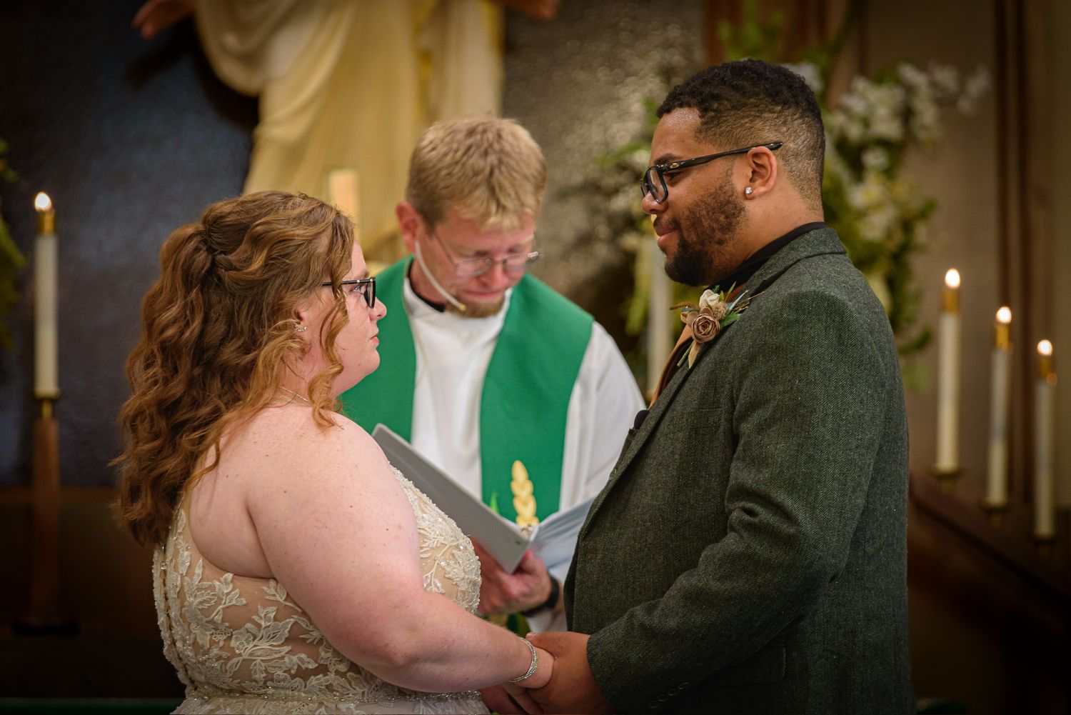 Bride and groom hold hands at church altar during wedding ceremony with officiant in green stole.